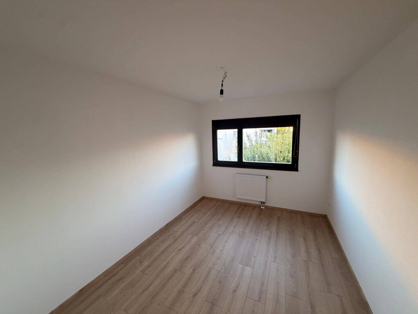 Helles Zimmer mit Laminatboden und Fenster, das eine freundliche und einladende Atmosphäre bietet.