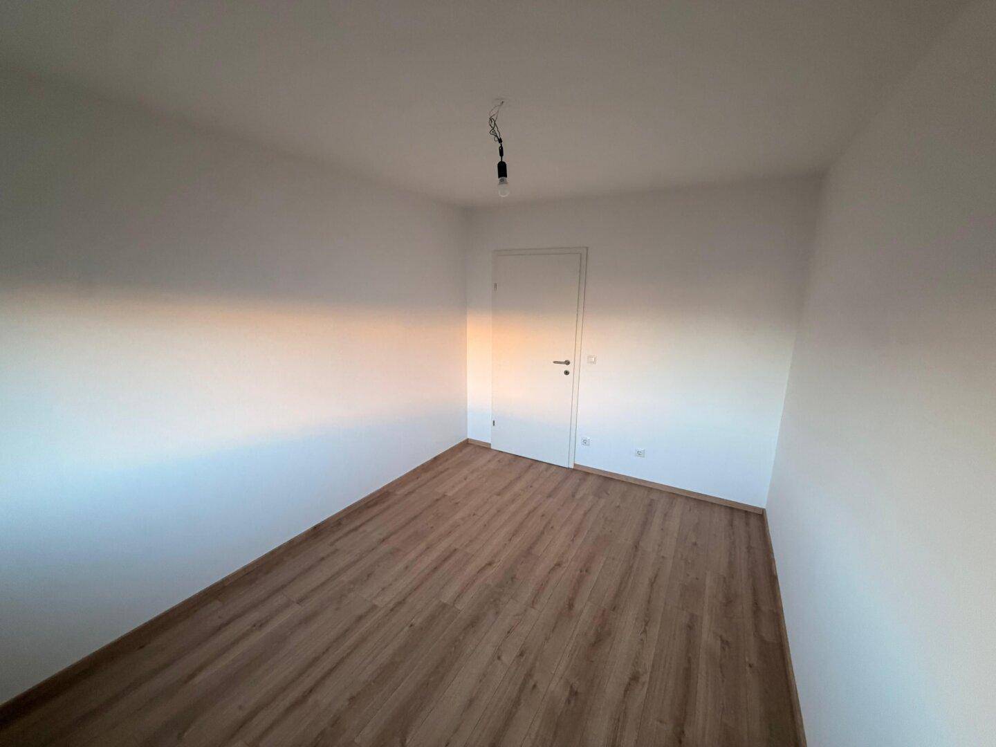 Neutral gestaltetes Zimmer mit Laminatboden und weiß gestrichenen Wänden, bereit zur individuellen Gestaltung.