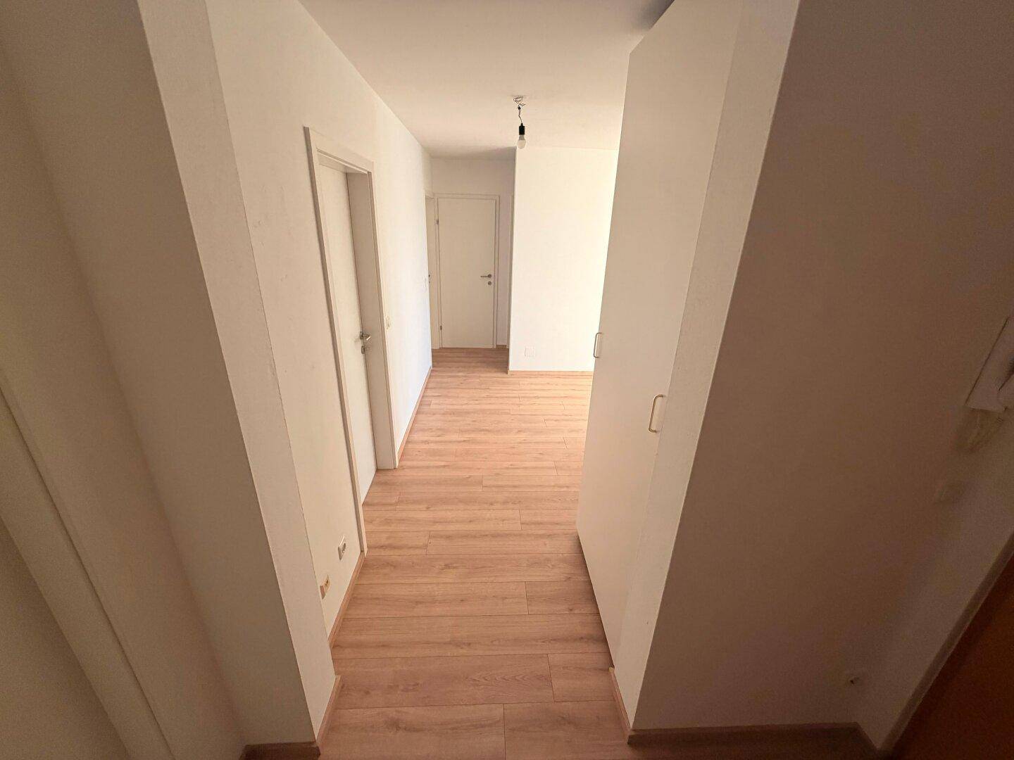 Langer, heller Flur mit Laminatboden, der zu den verschiedenen Räumen der Wohnung führt.
