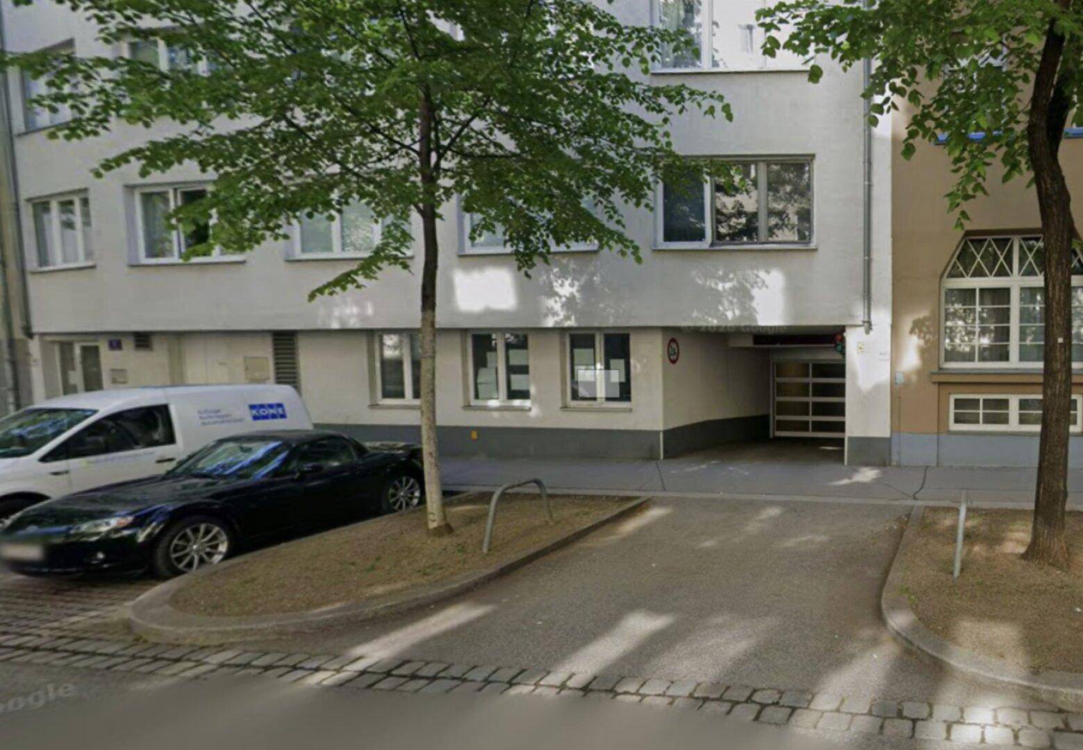 Gebäudefassade von der Straße aus gesehen mit Einfahrt zur Tiefgarage und Bäumen.