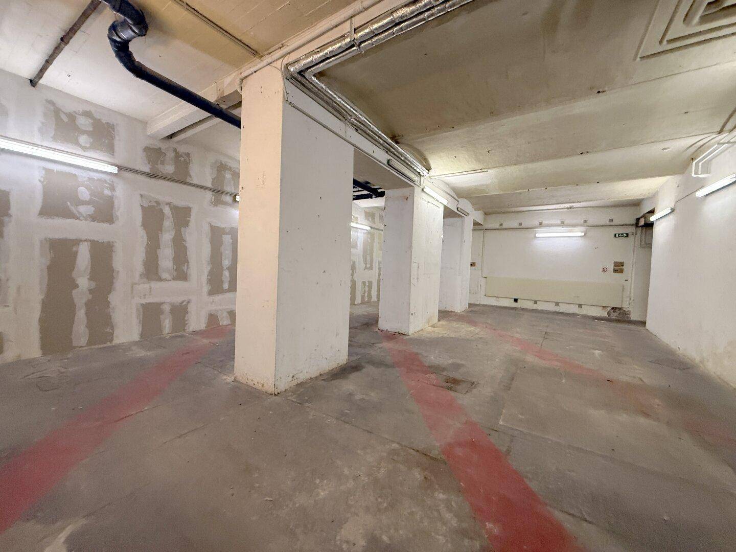 Leerer Gewerberaum mit Betonboden, tragenden Säulen und sichtbaren Rohrleitungen an der Decke.