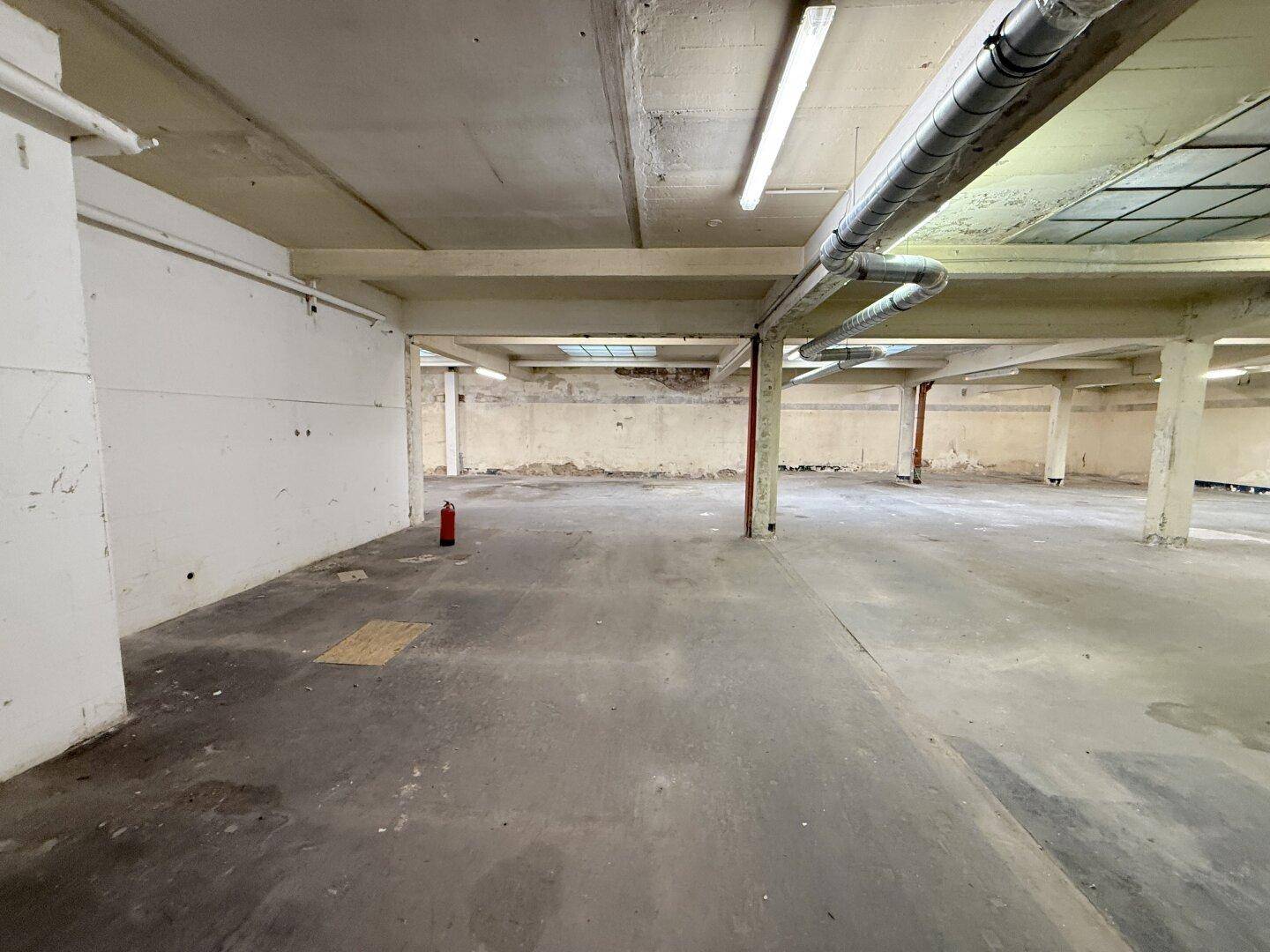 Geräumiger Industriebereich mit Betonboden, sichtbaren Trägern und einem Feuerlöscher, bereit zur Nutzung.