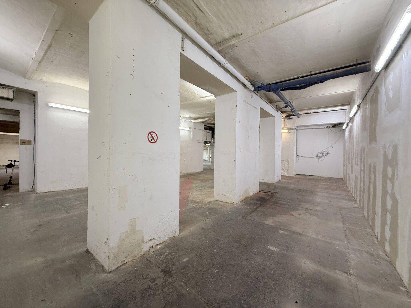Geräumiger Lagerraum mit Betonboden, tragenden Säulen und sichtbaren Installationen, gut beleuchtet.
