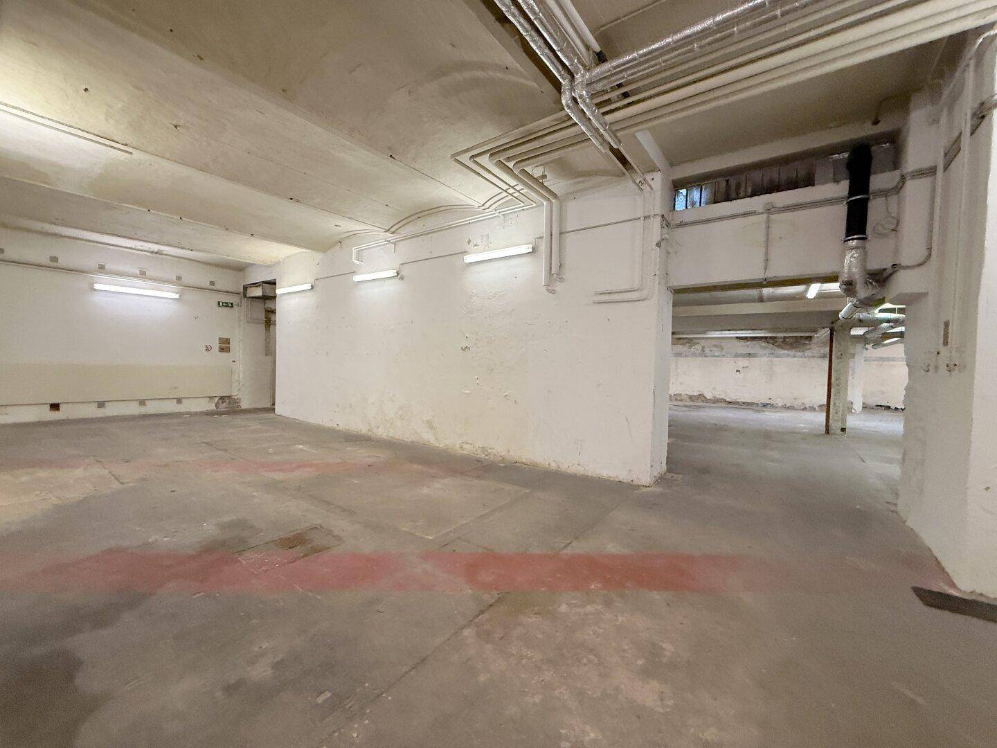 Weiterer Blick in den weitläufigen Lagerraum mit Betonboden und umfangreichen Deckeninstallationen.