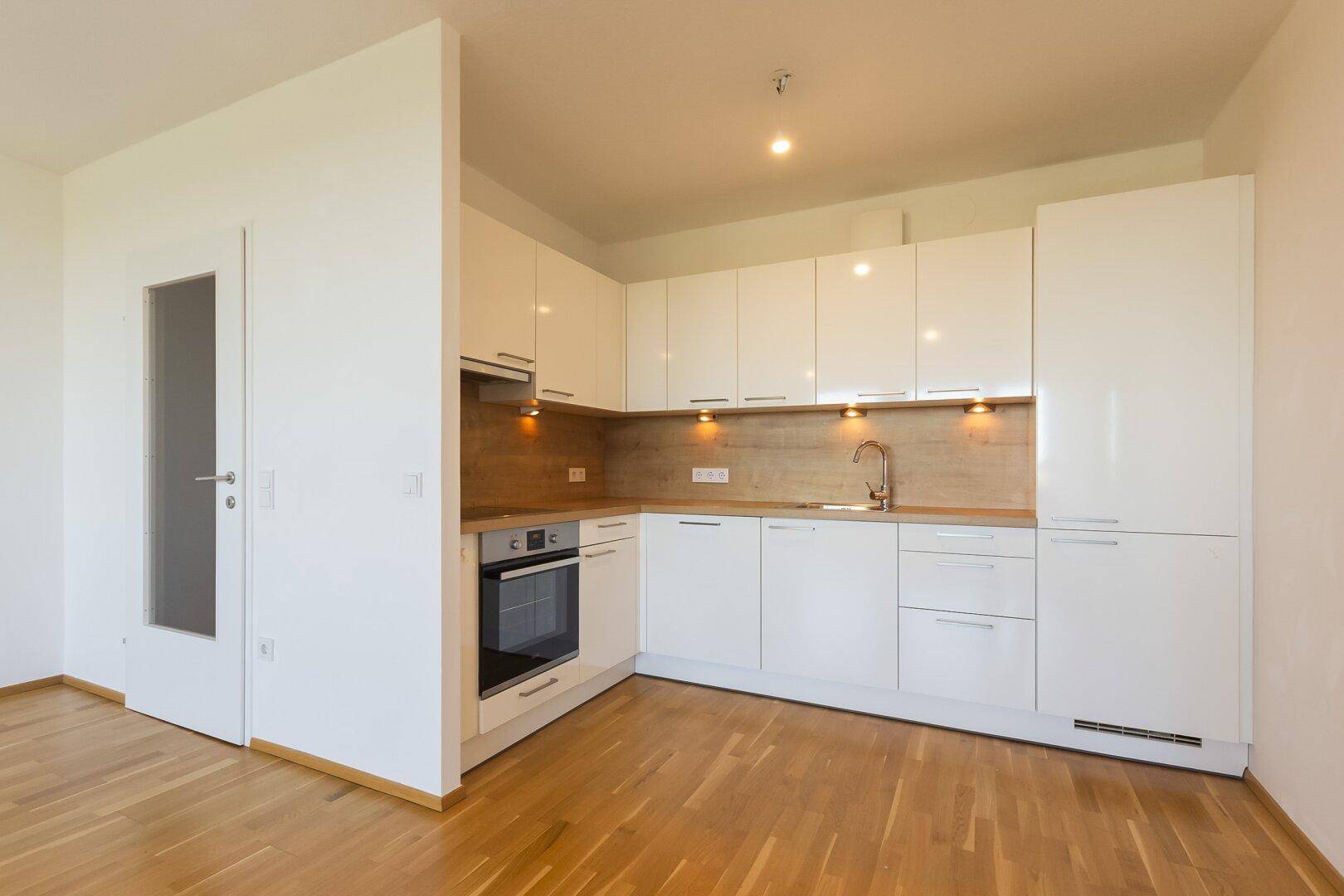Moderne Einbauküche mit weißen Hochglanzfronten, integrierten Geräten und Holz-Arbeitsplatte.