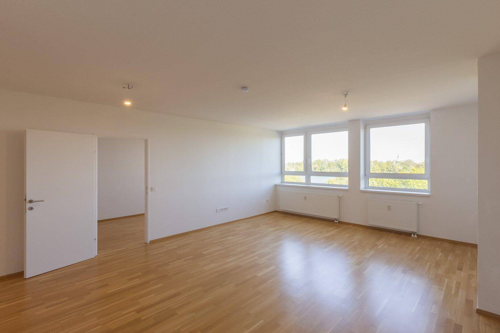 Weitläufiger, heller Wohnbereich mit Parkettboden und mehreren Fenstern, bietet viel Tageslicht.