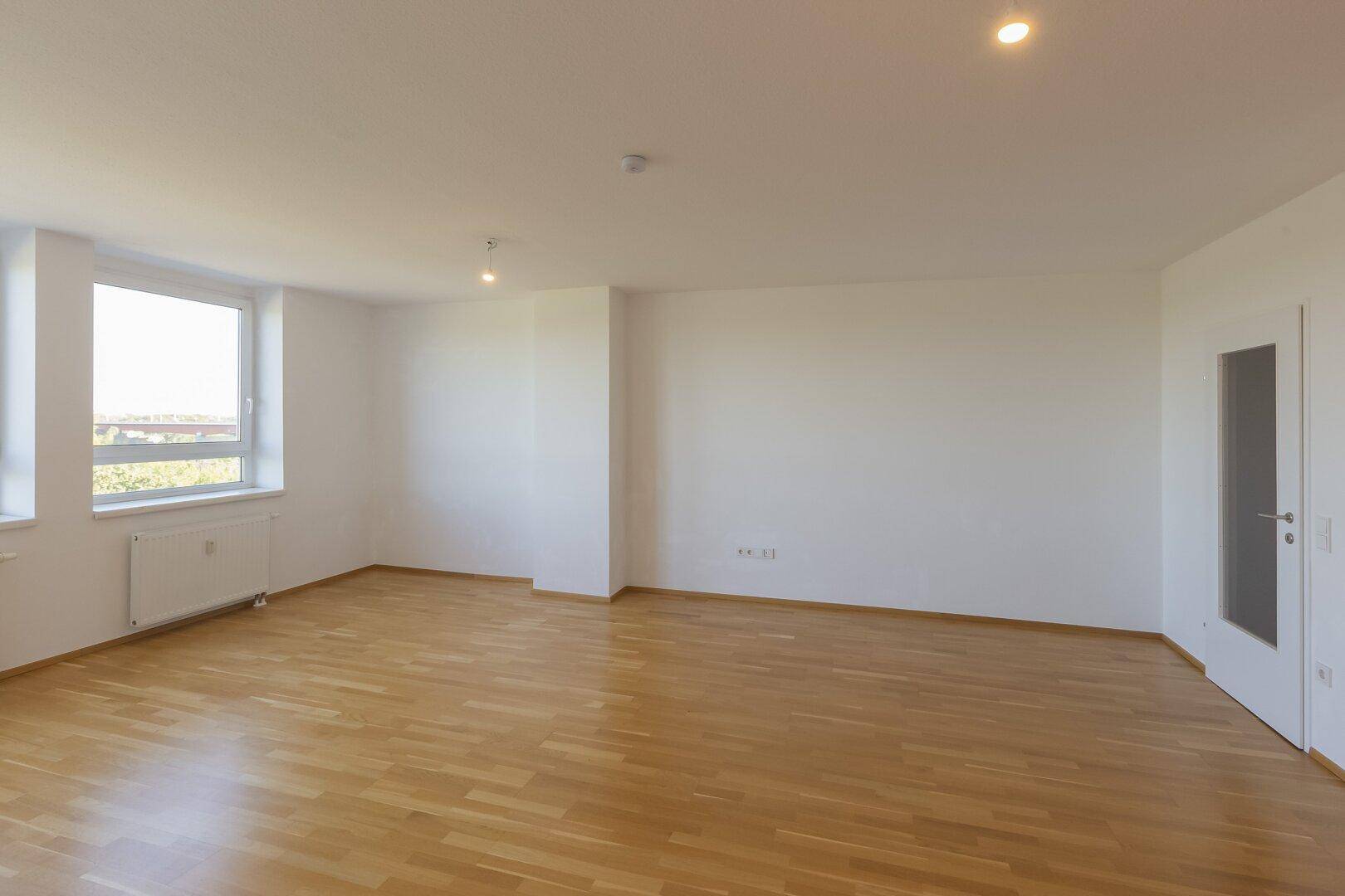 Leeres Zimmer mit hellem Parkettboden und Fenster, bietet viel Potenzial für individuelle Einrichtung.