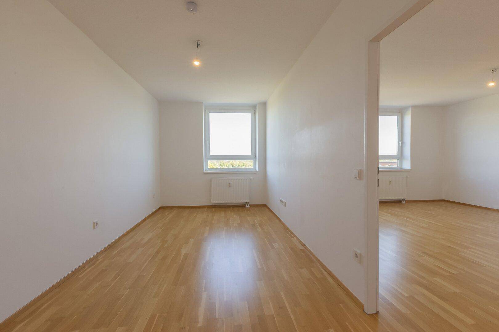 Geräumiges, unmöbliertes Zimmer mit hellem Parkettboden und Fenster, ideal für Schlaf- oder Arbeitsbereich.