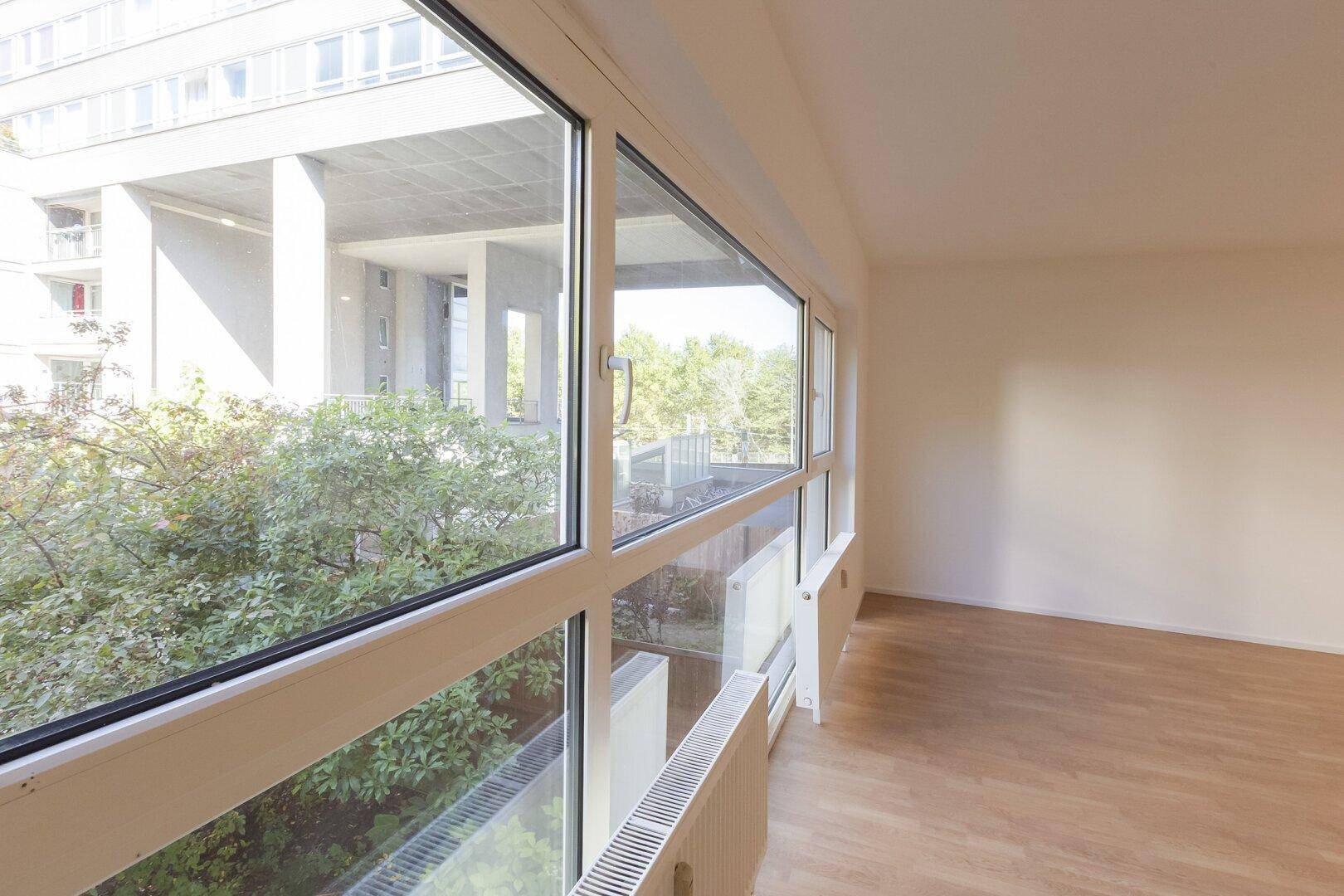 Große Fensterfront im Wohnzimmer bietet einen Ausblick auf Bäume und umliegende Gebäude.