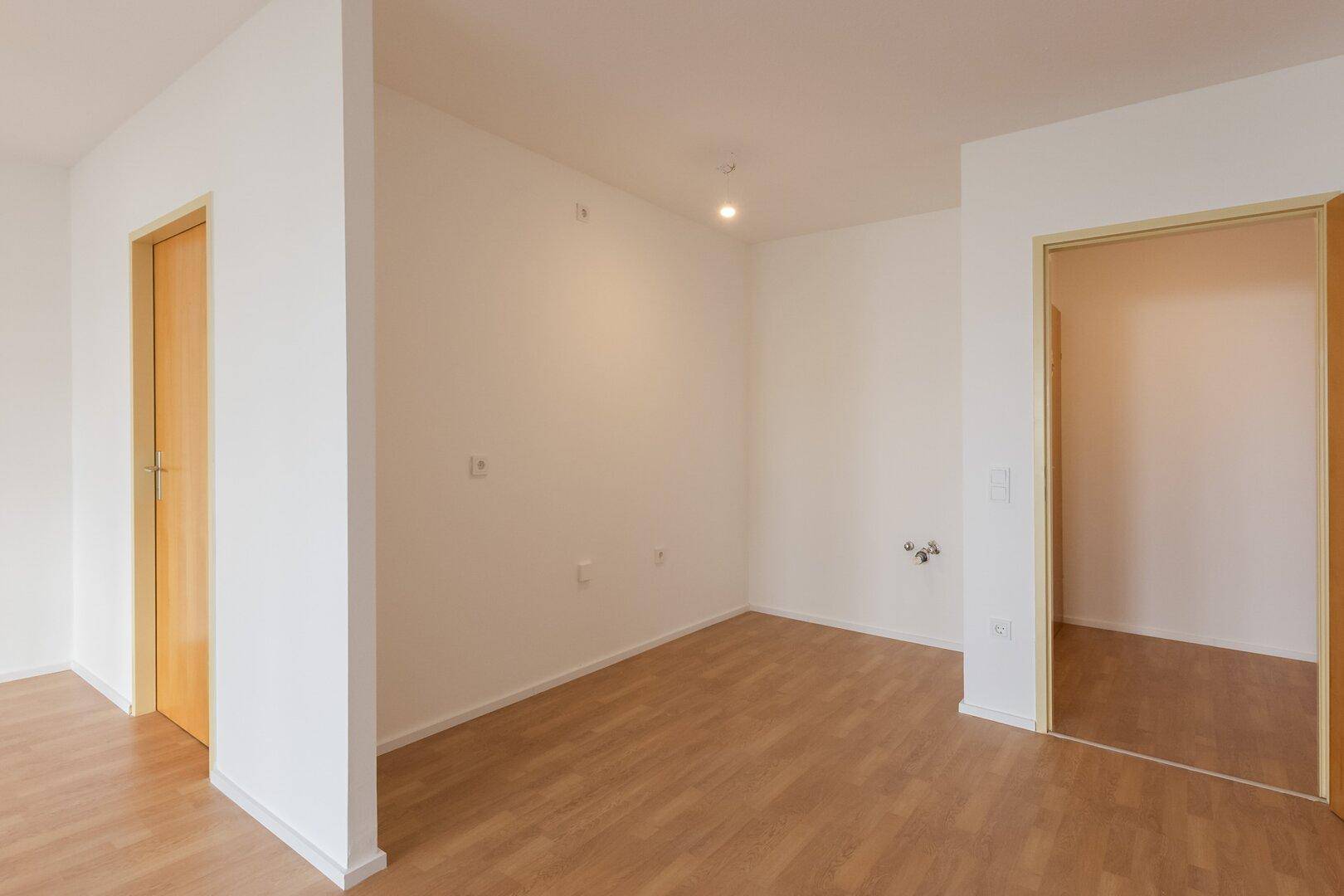 Leerer Raum mit zwei Holztüren und hellem Laminatboden, vielseitig nutzbar.