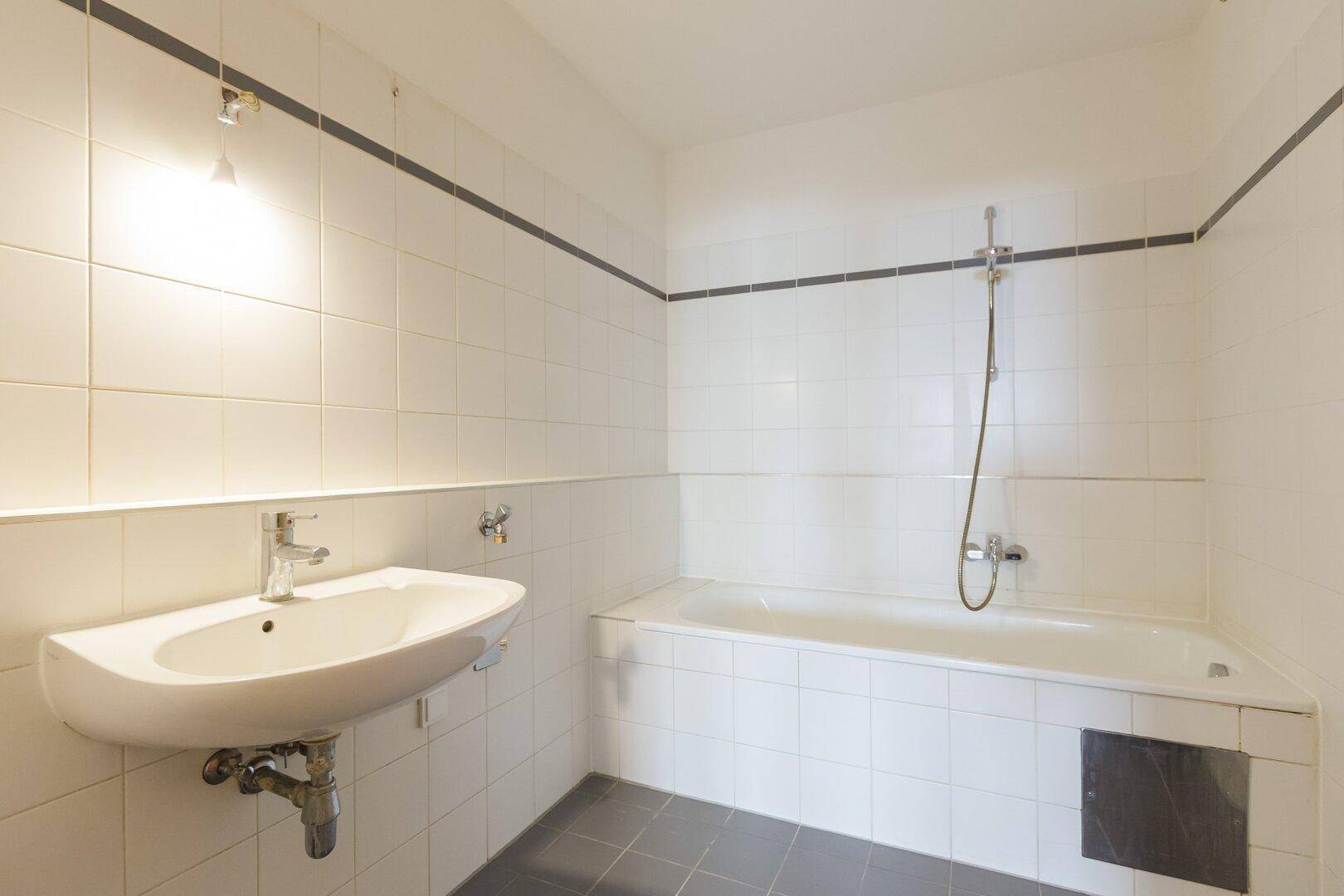 Funktionales Badezimmer mit weiß gefliesten Wänden, Badewanne und einem einzelnen Waschbecken.