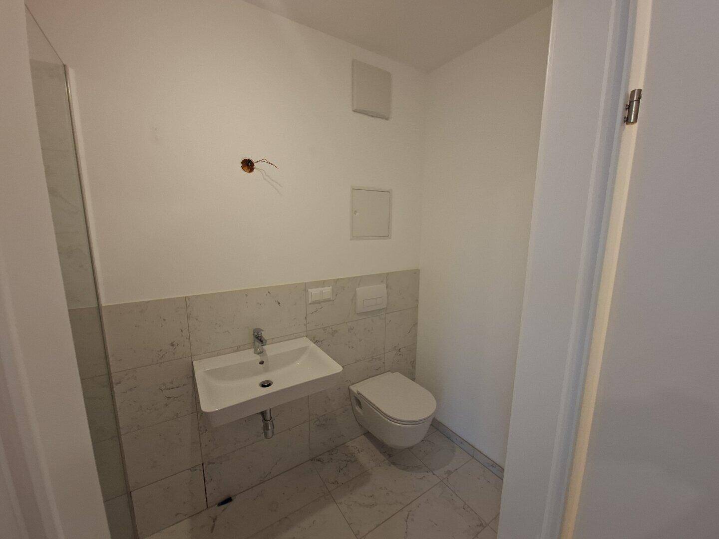 Helles Gäste-WC mit wandhängendem WC, Waschbecken und modernen Fliesen.