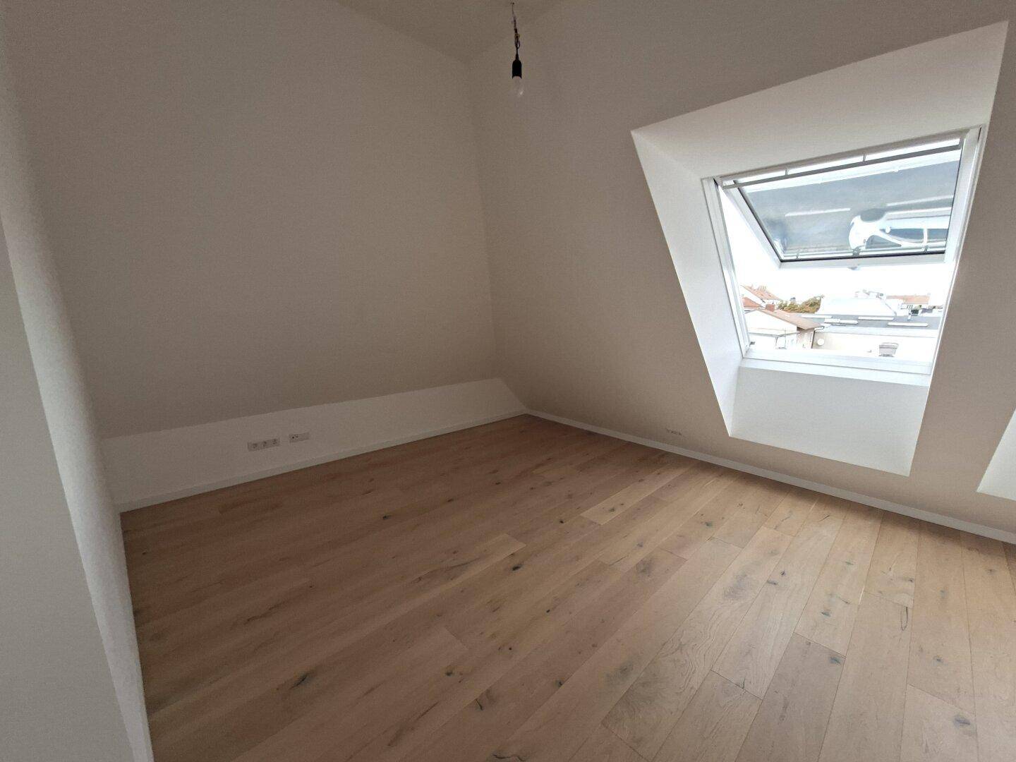 Heller Raum im Dachgeschoss mit Holzboden und einem großen Dachfenster.