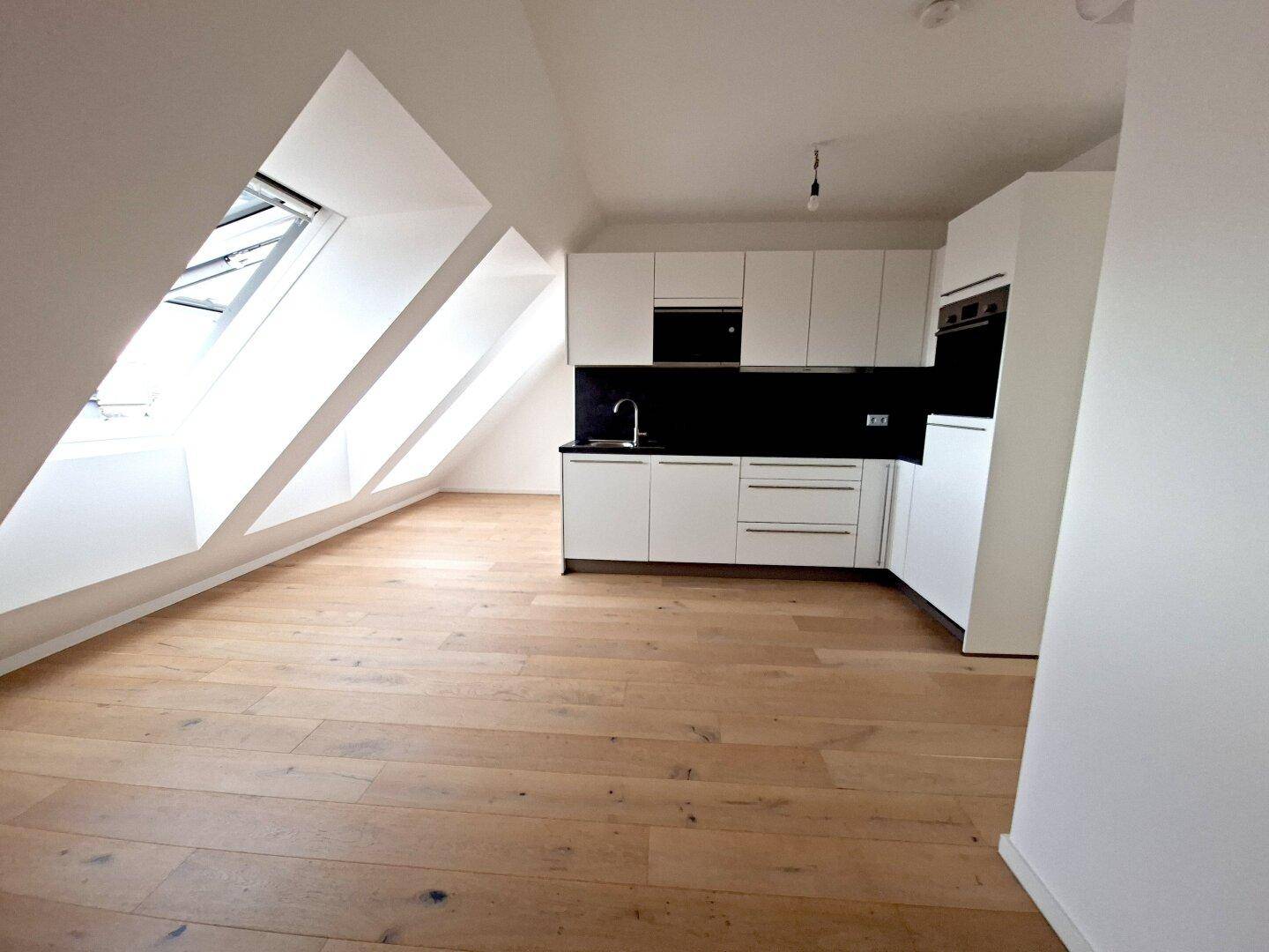 Offene Küchenzeile in einem hellen Dachgeschossraum mit Holzboden und schrägen Wänden.