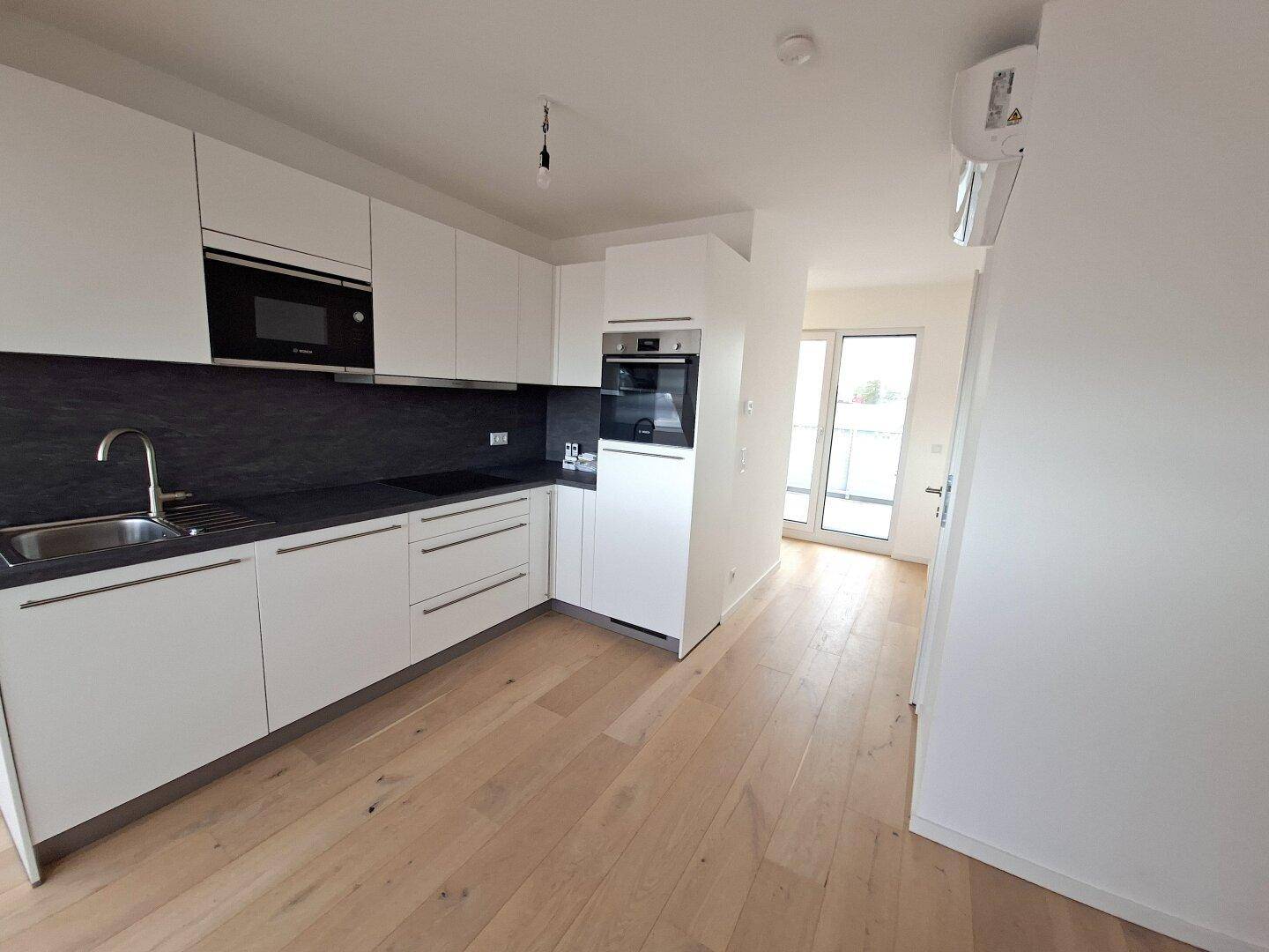 Moderne Küchenzeile mit weißen Schränken und Zugang zu einem Balkon oder einer Terrasse.