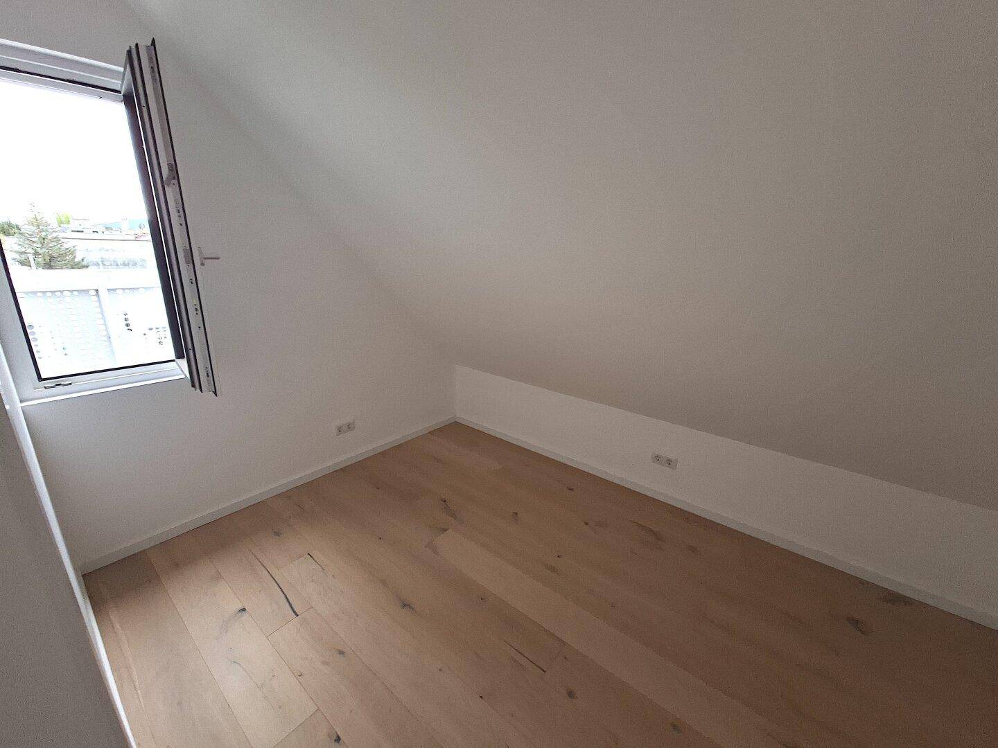Kleiner, heller Raum im Dachgeschoss mit Holzboden und einem Fenster.