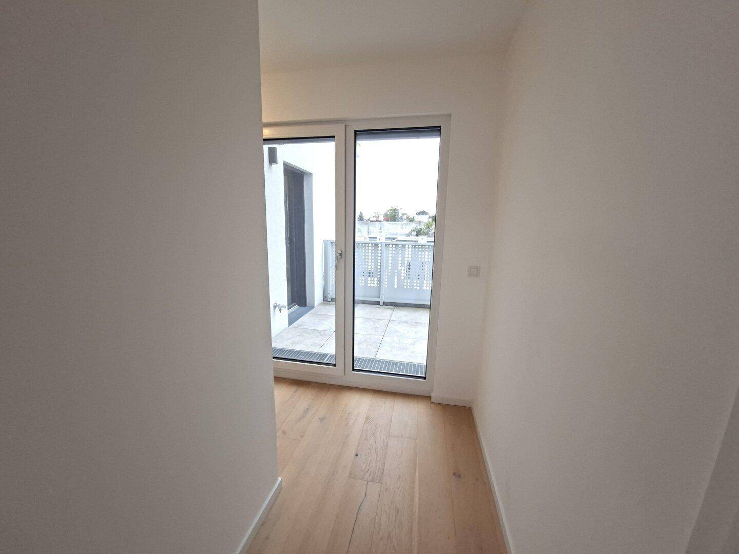 Heller Flur mit Holzboden und großen Fenstertüren, die zu einem Außenbereich führen.