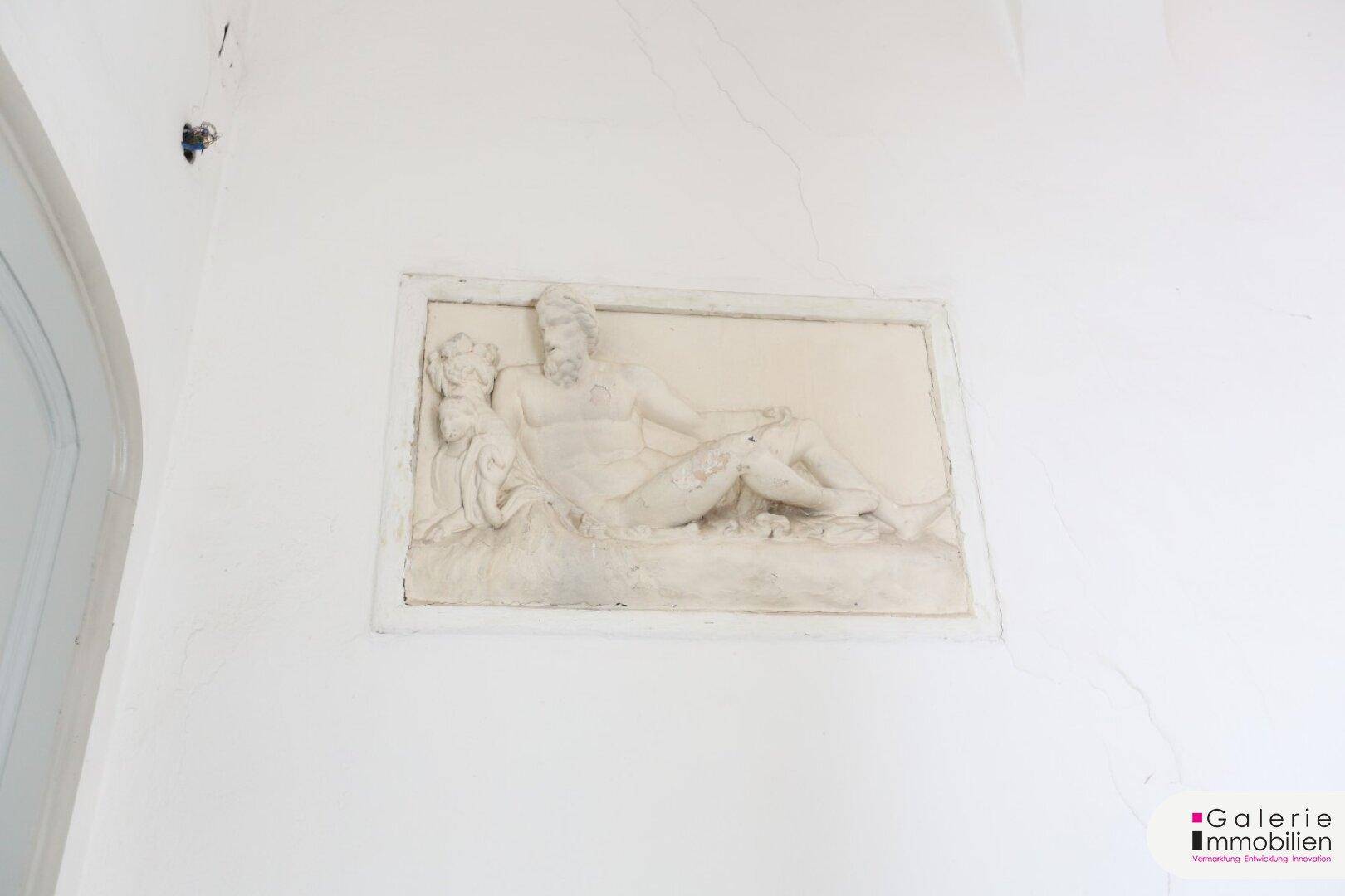 Dekoratives Wandrelief mit klassischer Darstellung an einer hellen Wand.