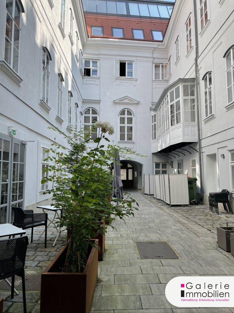 Heller Innenhof mit Sitzgelegenheiten und Pflanzen, umgeben von weißen Gebäudefassaden.