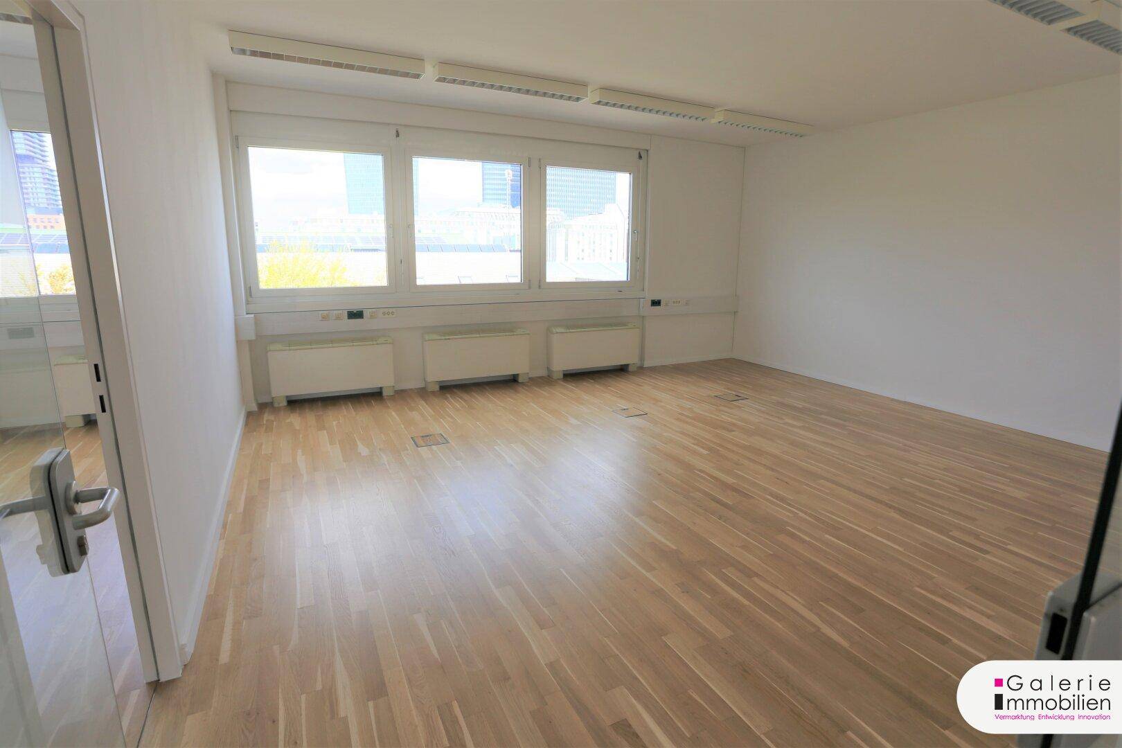 Geräumiges und helles Büro mit Holzboden und einer Reihe großer Fenster, die einen weiten Ausblick bieten.