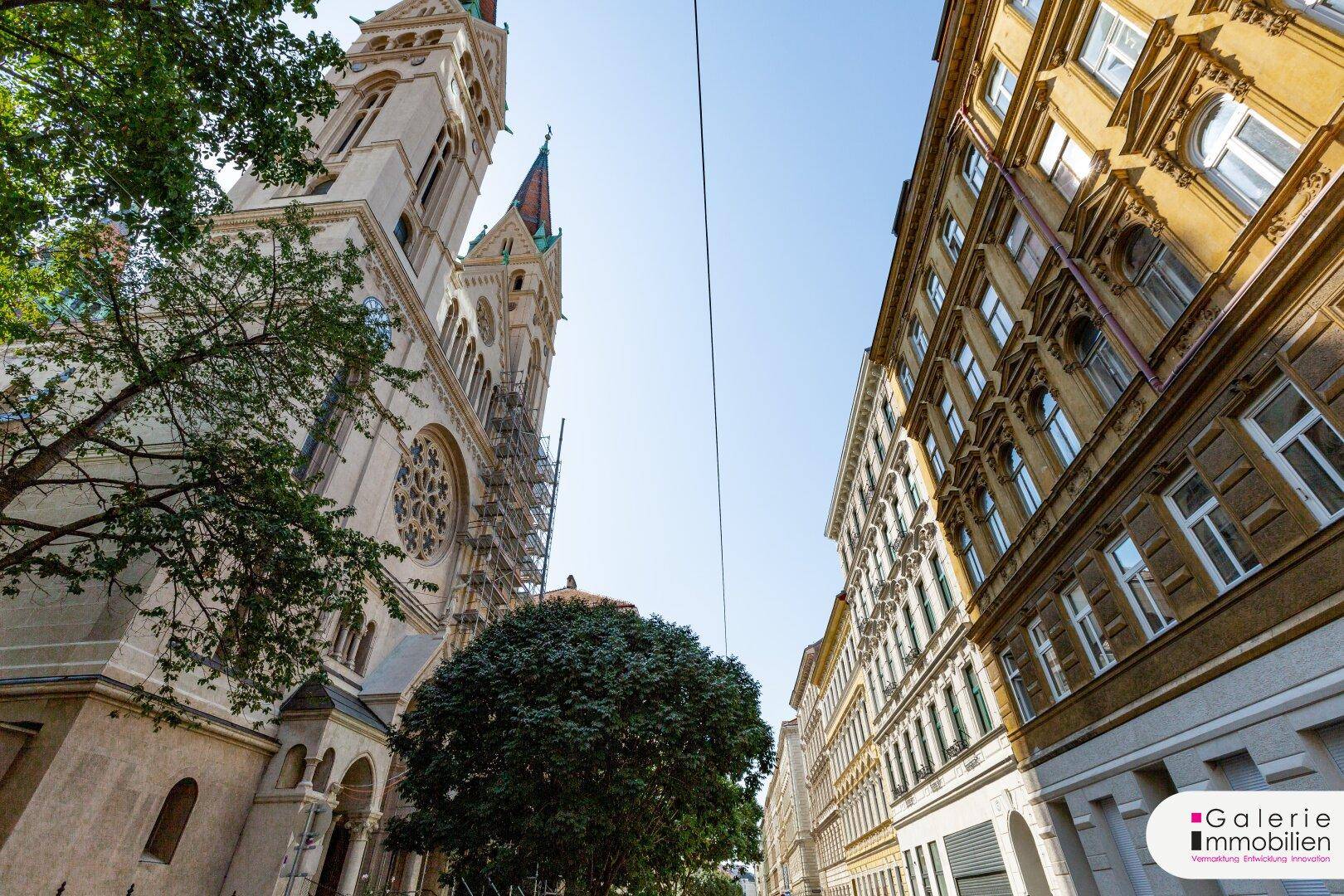 Historische Straße mit einer imposanten Kirche und klassischen Gebäuden unter blauem Himmel.