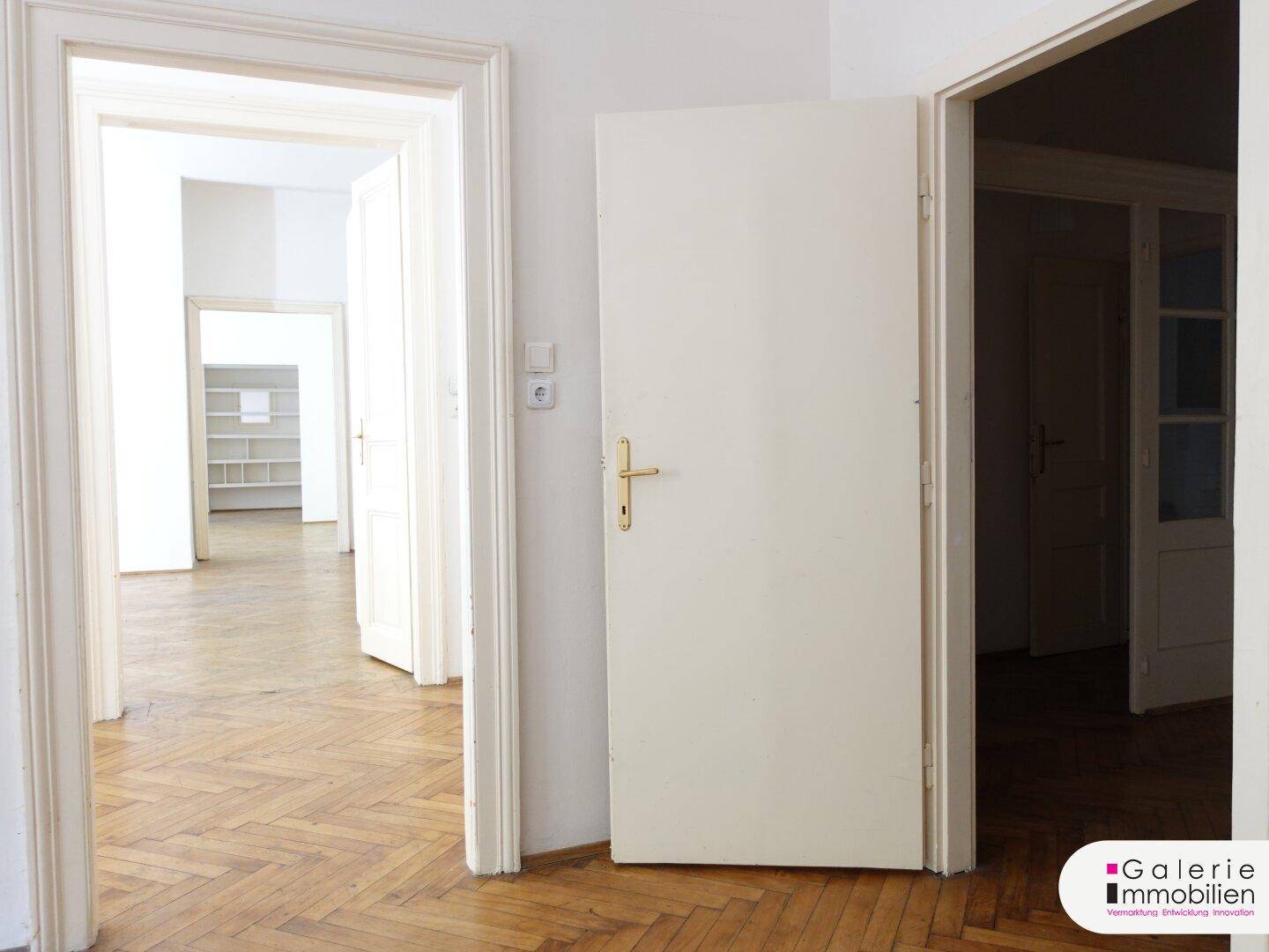 Flur mit Fischgrätparkett und einer Reihe offener Türen, die einen Blick in weitere Räume ermöglichen.