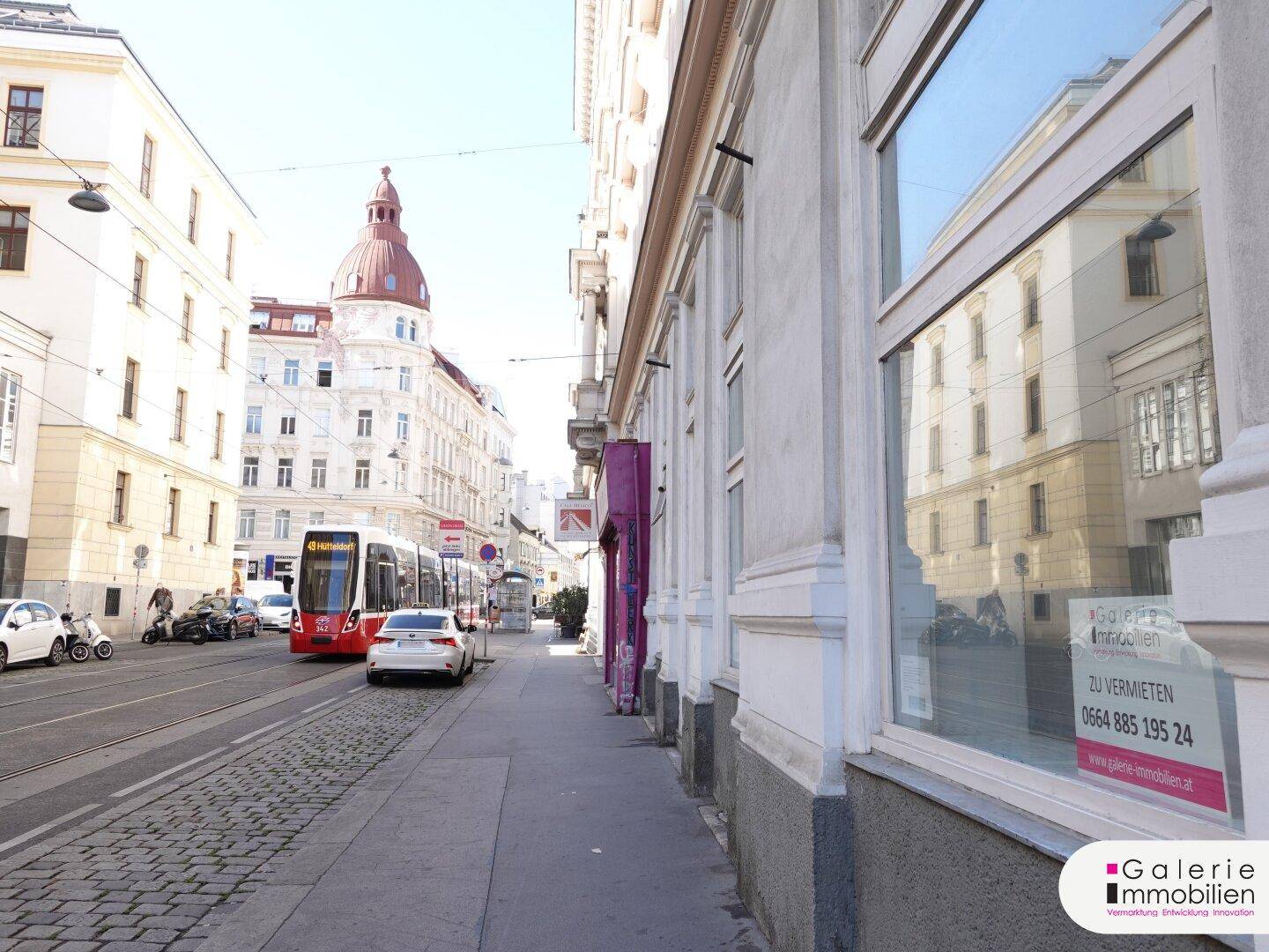 Belebte Stadtstraße mit einer Straßenbahn, parkenden Autos und Gebäuden im Hintergrund.