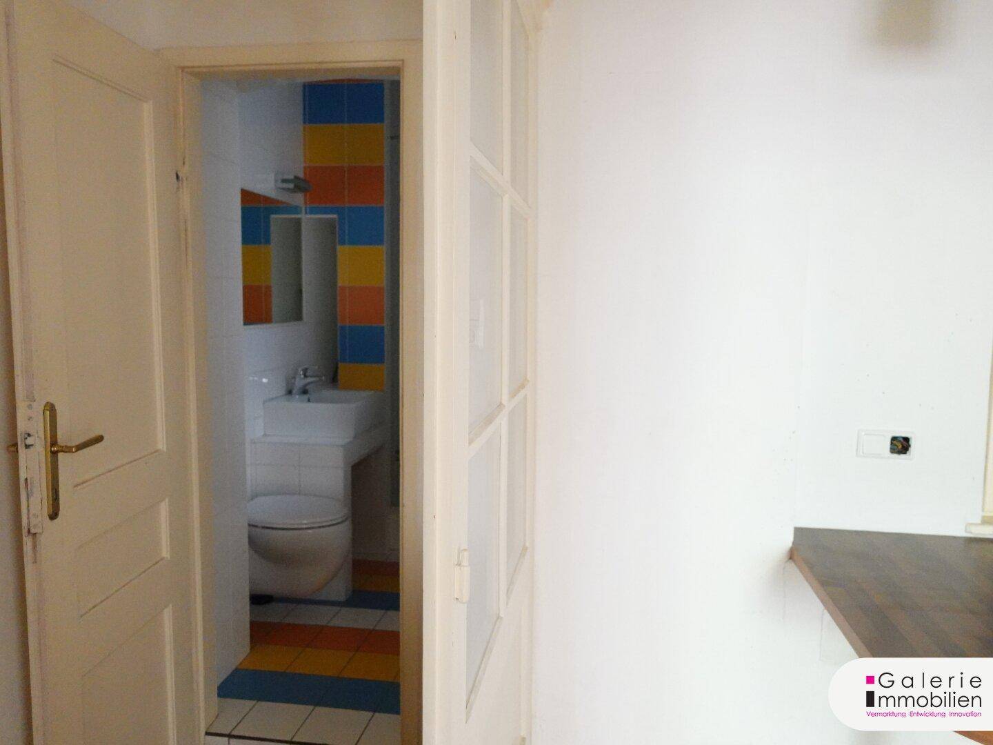 Badezimmer mit WC, Waschbecken und farbenfrohen Fliesen an den Wänden und auf dem Boden.
