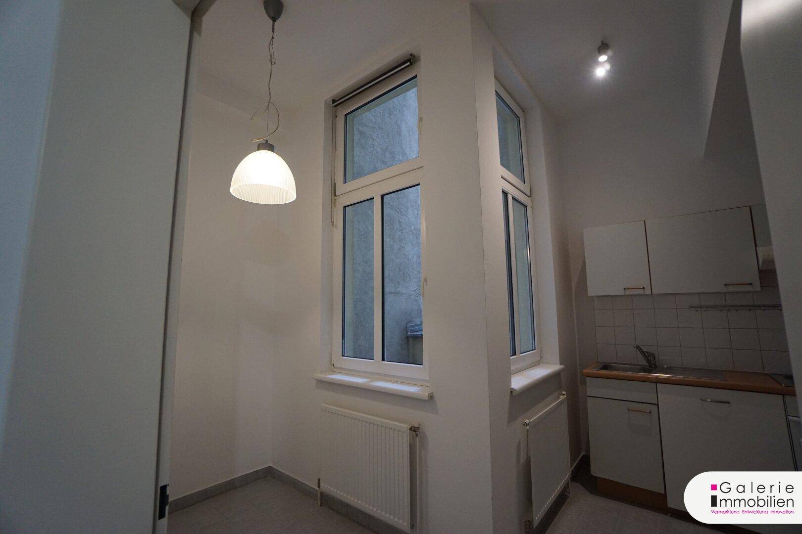 Helle Küchenecke mit Fenster und Pendelleuchte, die Tageslicht hereinlässt.