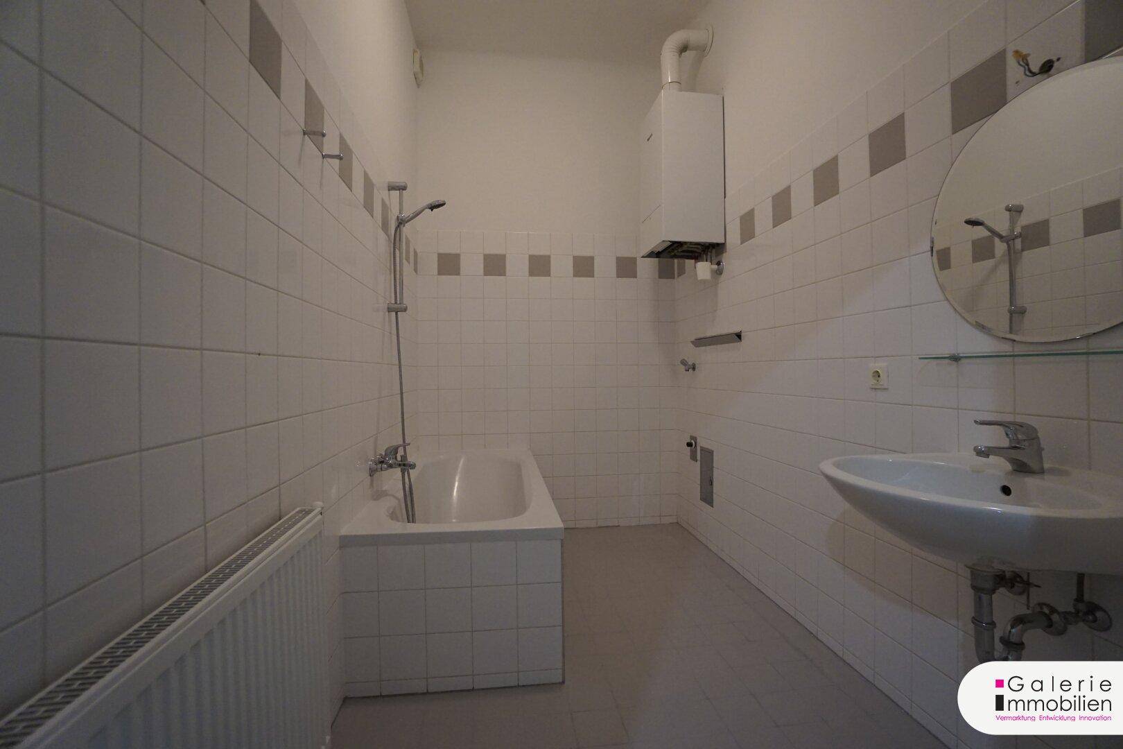 Badezimmer mit Badewanne, Waschbecken und Wandfliesen in Weiß und Grau.