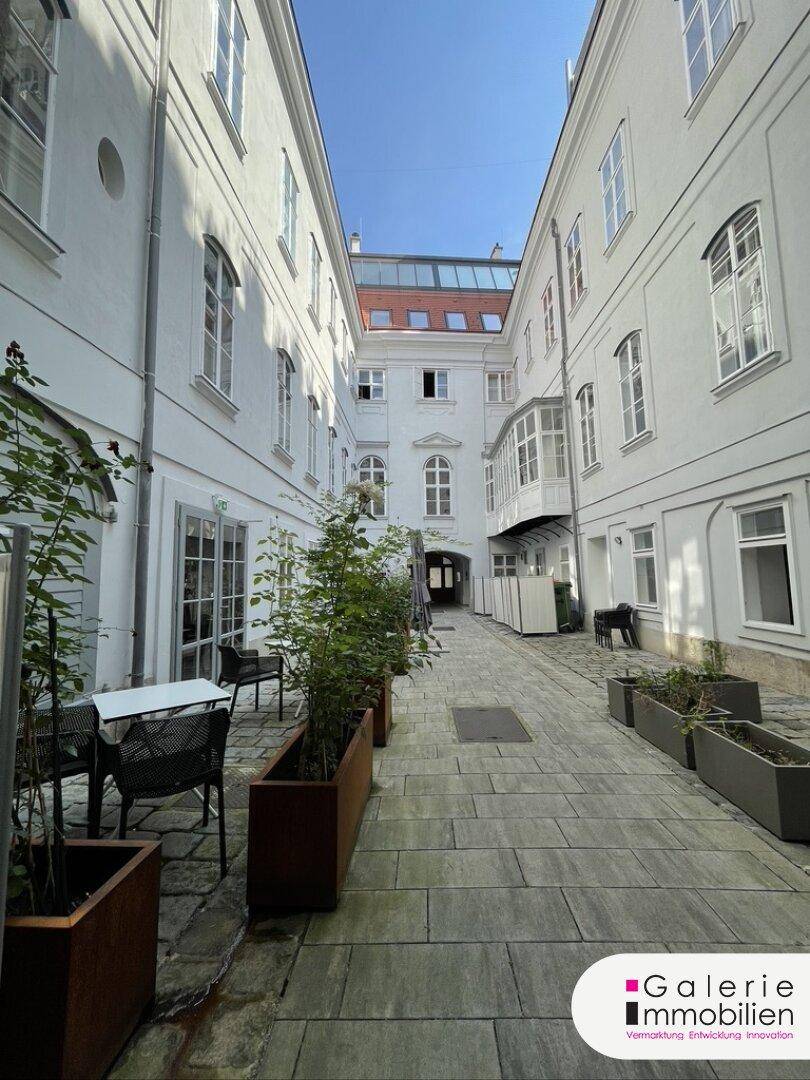 Heller Innenhof mit weiß gestrichenen Gebäuden, gepflastertem Boden und einer gemütlichen Sitzgelegenheit im Freien.