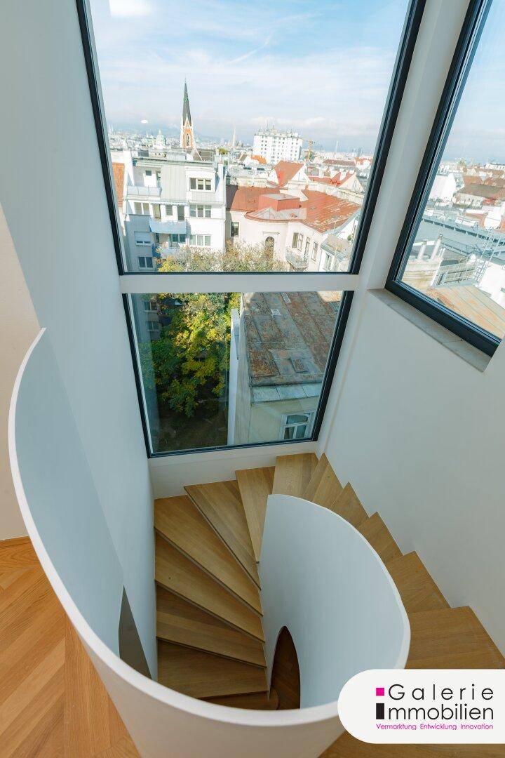 Elegante Wendeltreppe mit großen Fenstern, die einen weiten Blick über die Stadt bieten.
