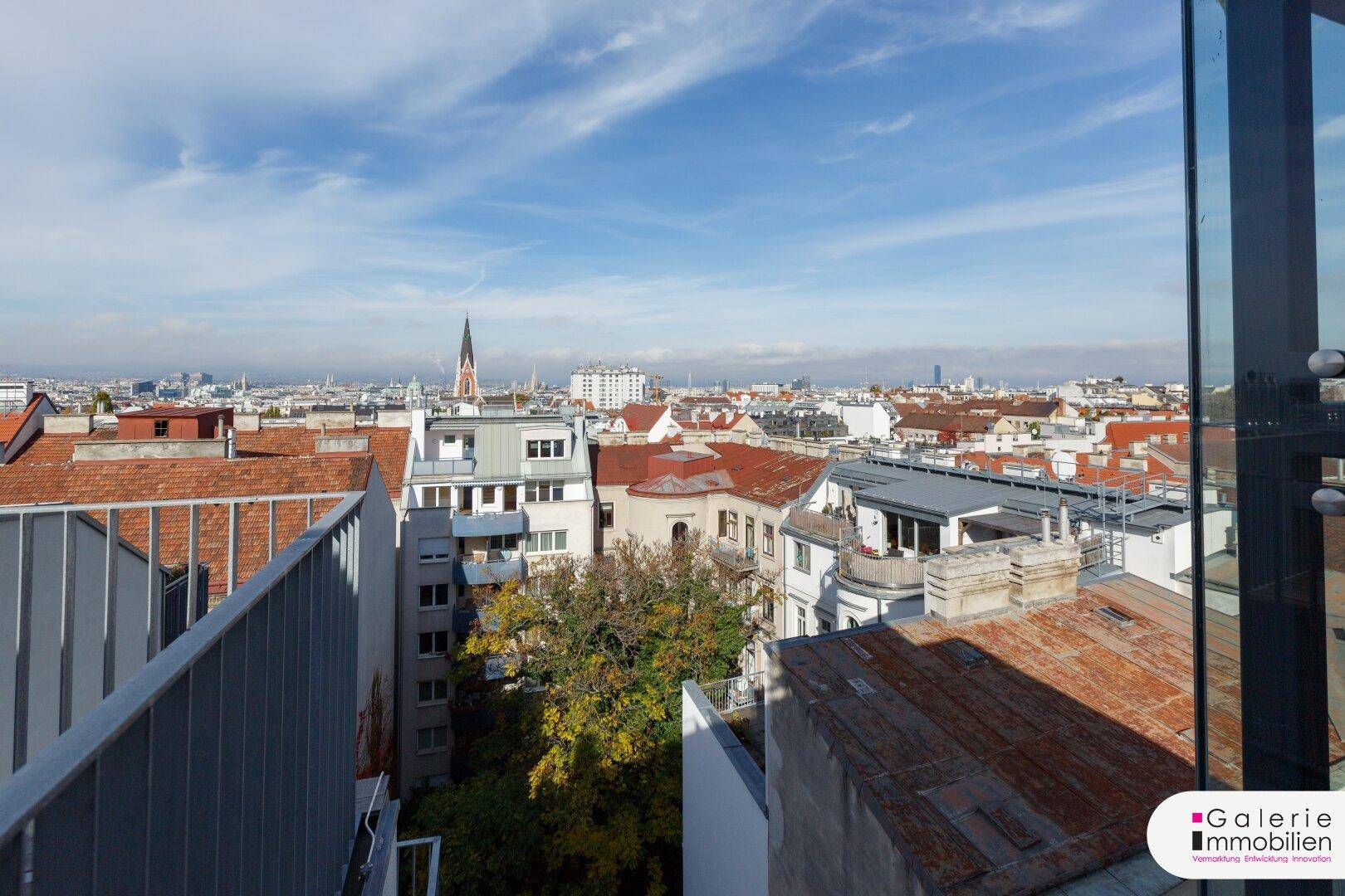 Weitläufiger Blick über die Dächer Wiens mit historischem Kirchturm und blauem Himmel.