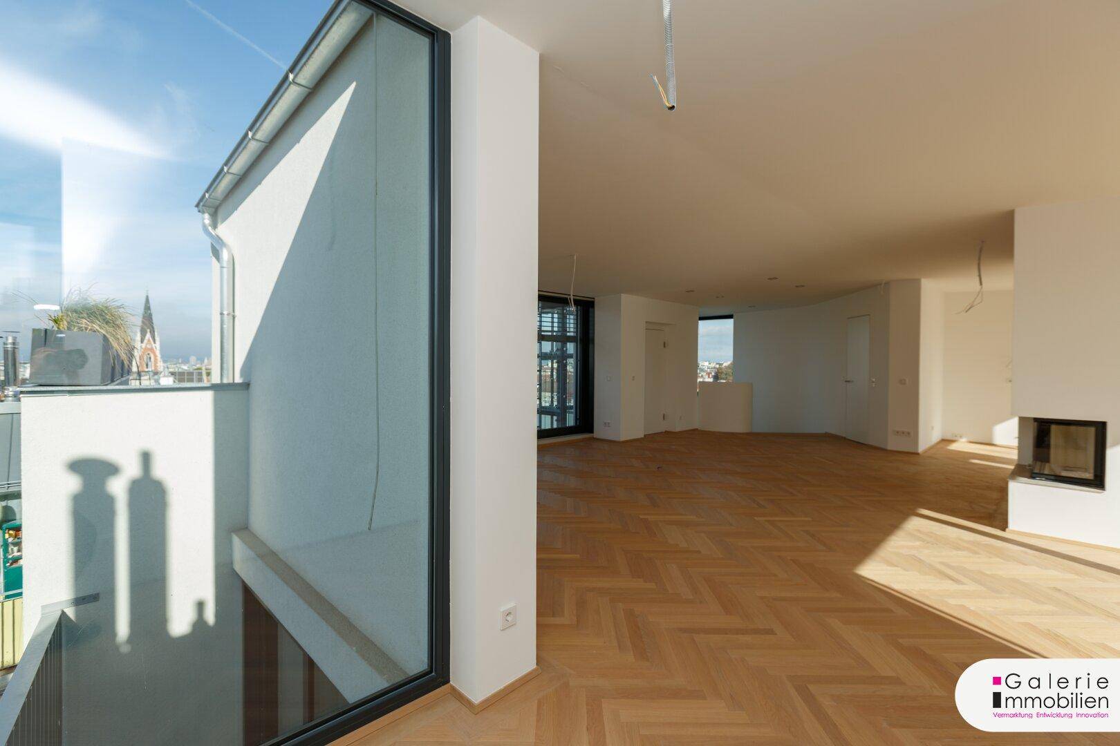 Lichtdurchfluteter Wohnbereich mit Fischgrätparkett und Kamin, bietet Zugang zur Dachterrasse.