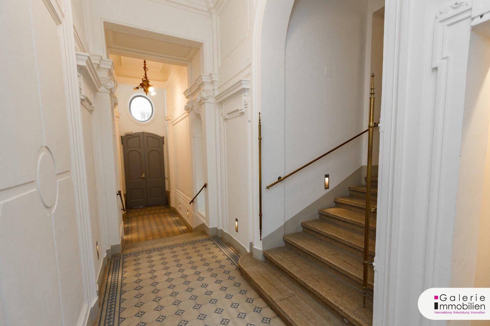 Eleganter Eingangsbereich mit historischen Fliesen, Stuckdecken und einer geschwungenen Treppe.