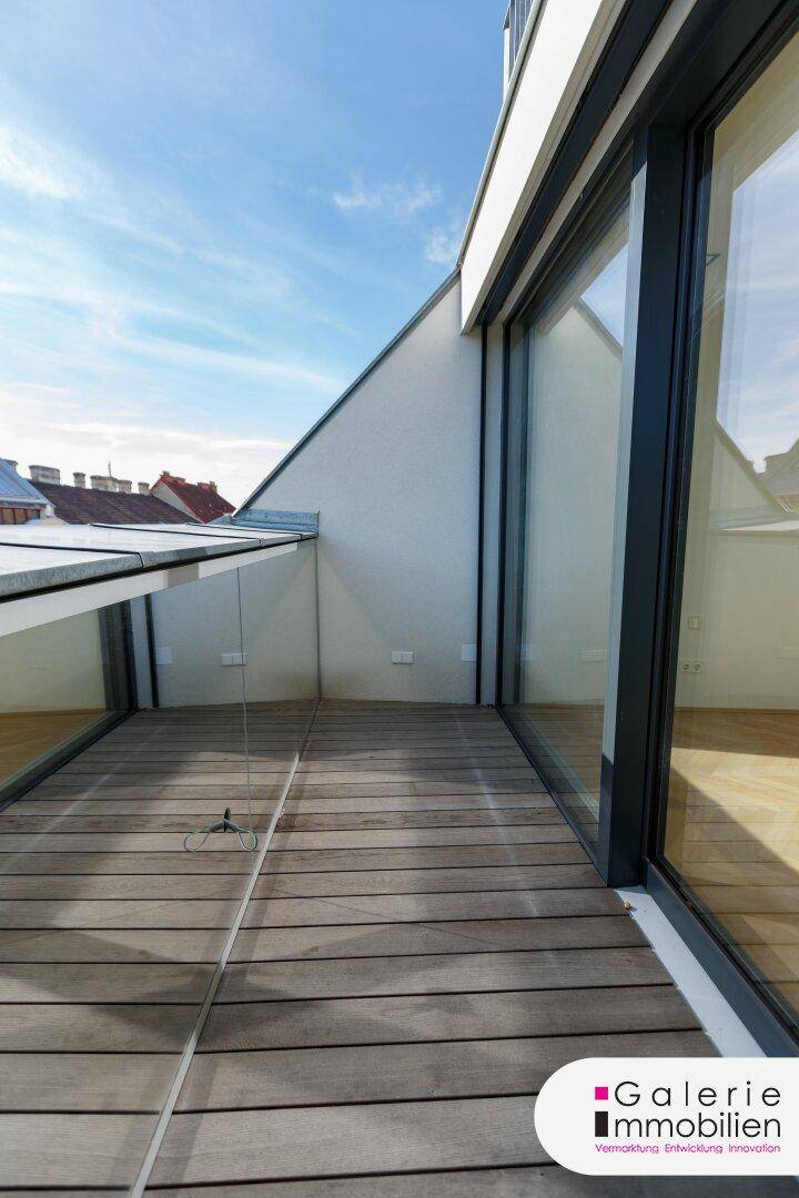 Überdachte Terrasse mit Holzboden und Glasgeländer, die einen geschützten Außenbereich schafft.