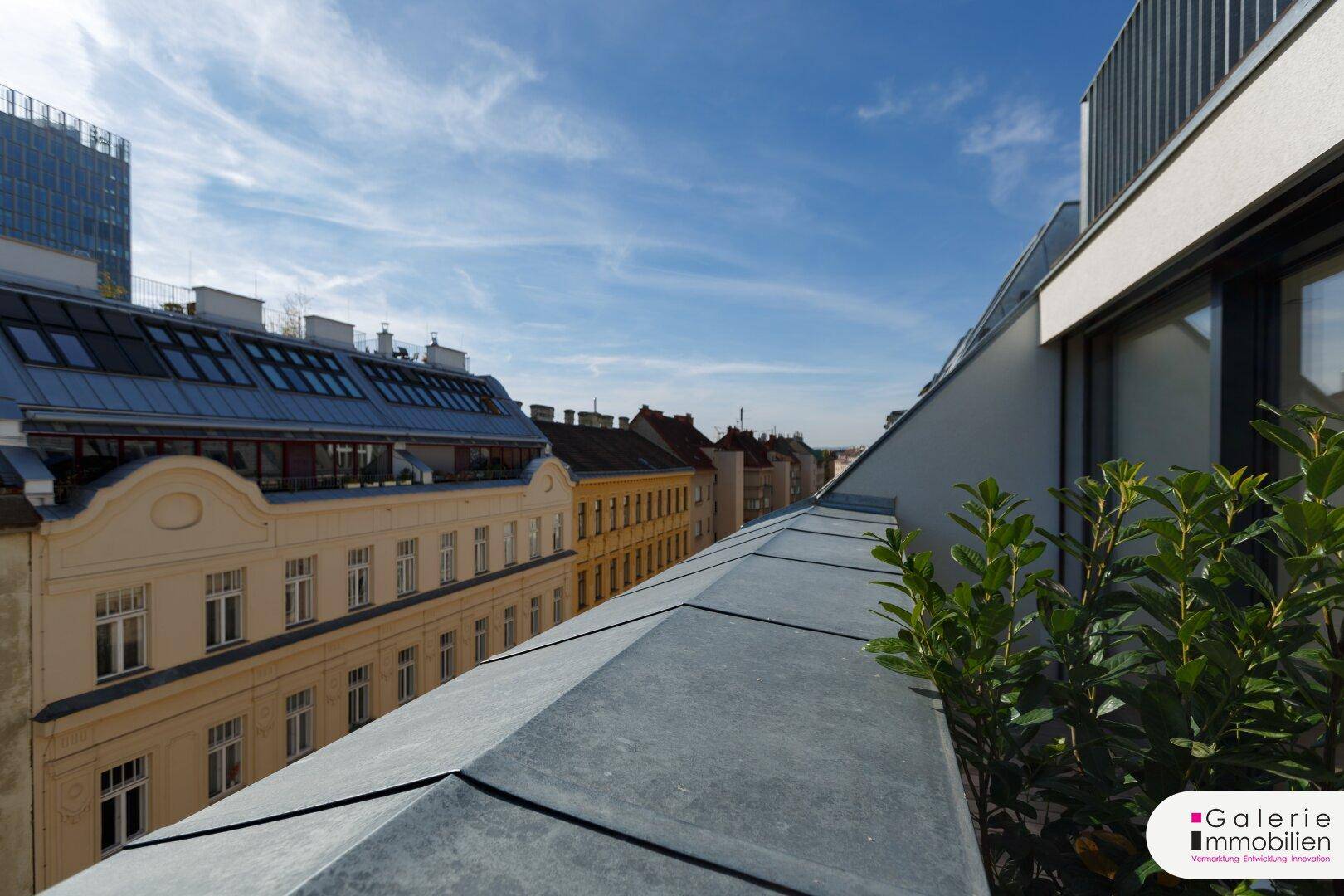 Blick über die Dächer der Stadt mit blauem Himmel und modernen Gebäudeelementen.