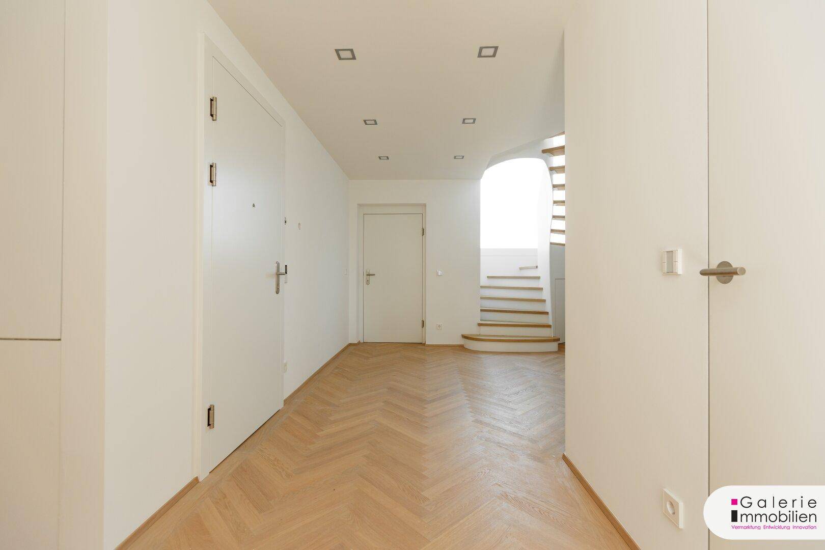 Geräumiger Flur mit hellem Fischgrätparkett und Zugang zu verschiedenen Räumen und einer Treppe.
