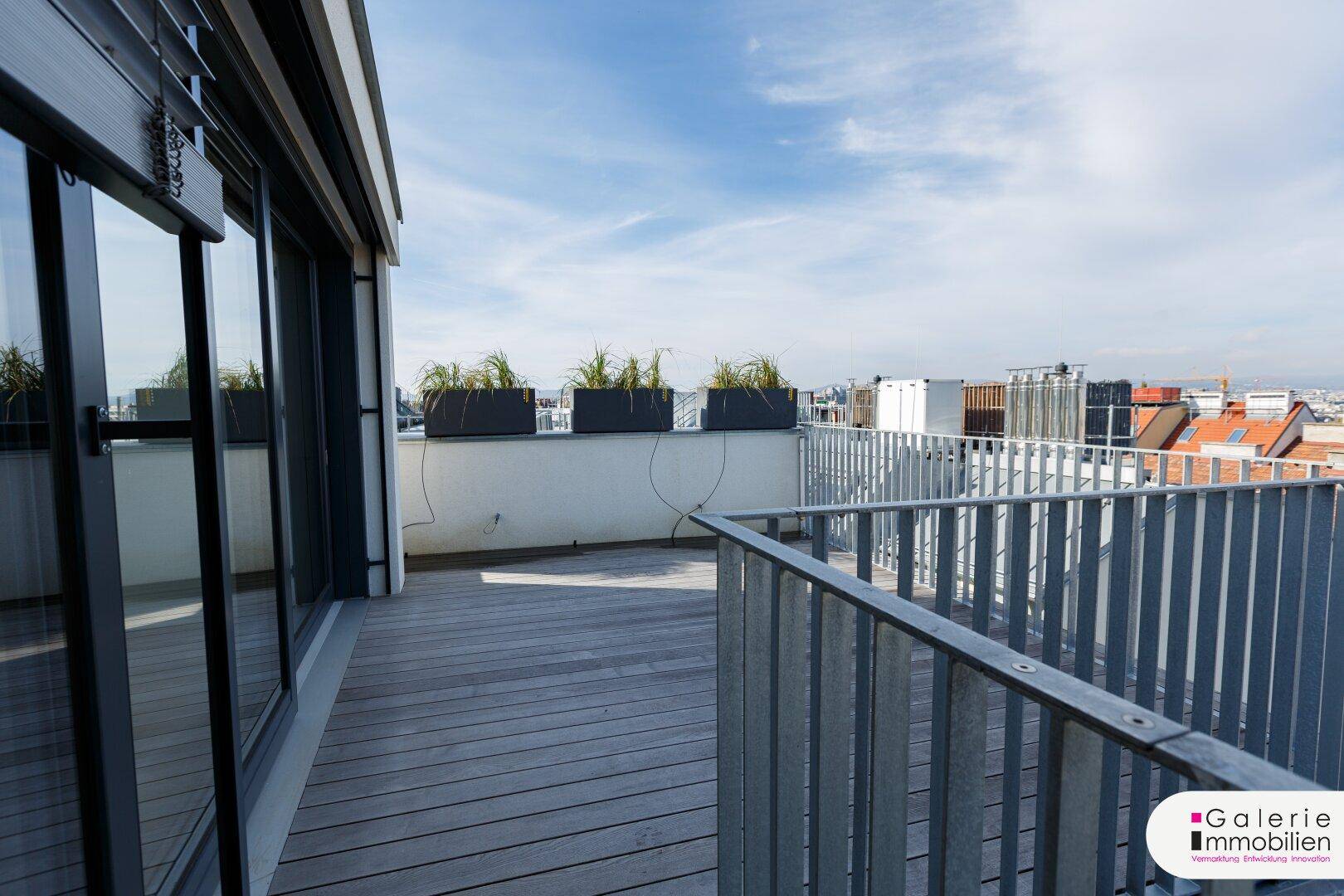 Geräumige Dachterrasse mit Holzboden und Pflanzkübeln, die einen weiten Stadtblick bietet.