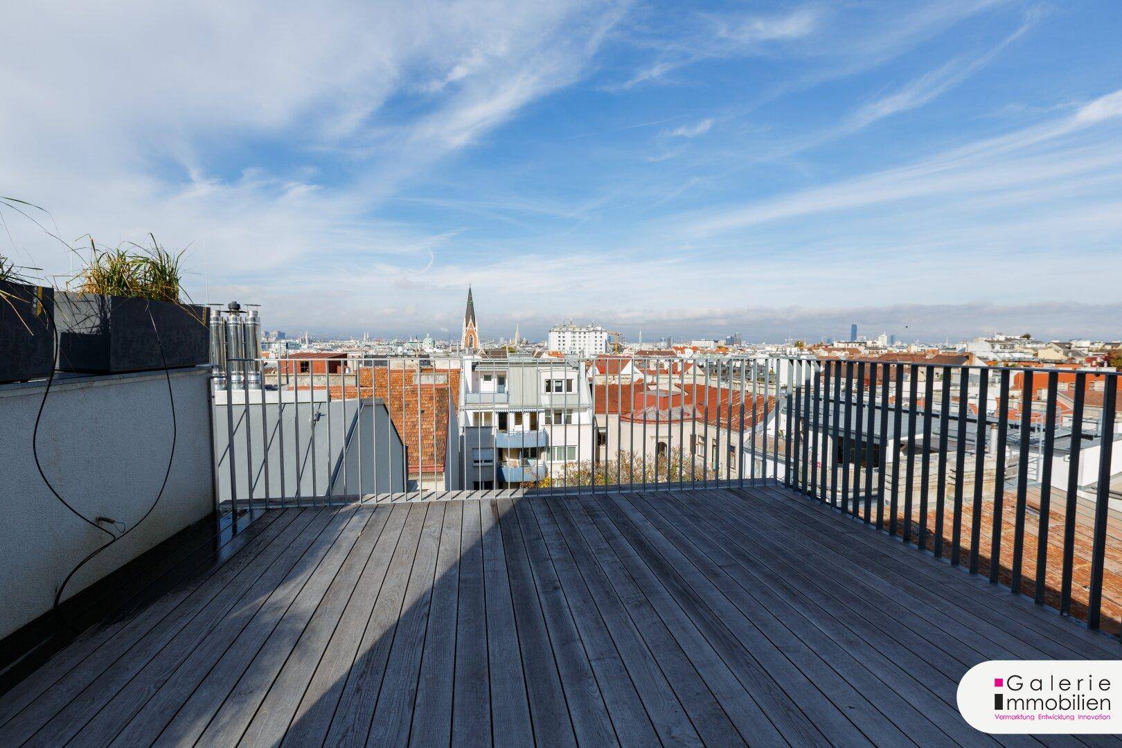 Große Dachterrasse mit Holzboden und weitem Blick über die Stadt und die umliegenden Dächer.