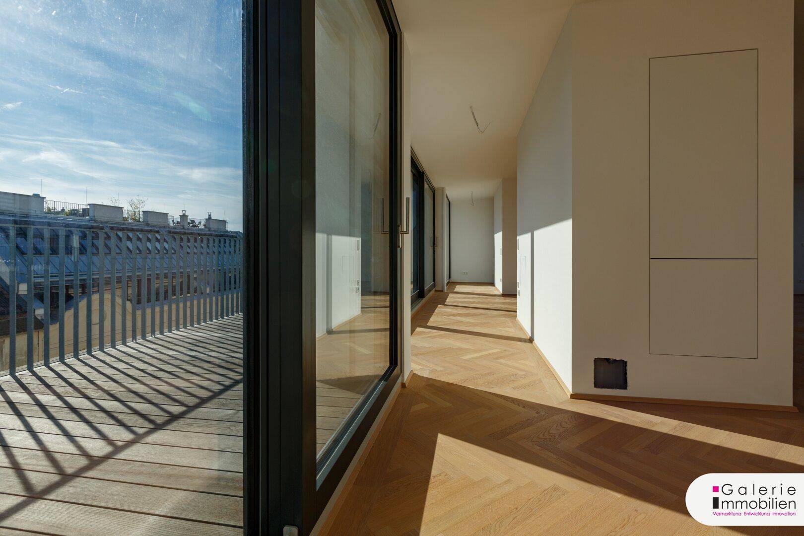 Heller Flur mit Fischgrätparkett und großen Fenstern, die zu einer Dachterrasse führen.