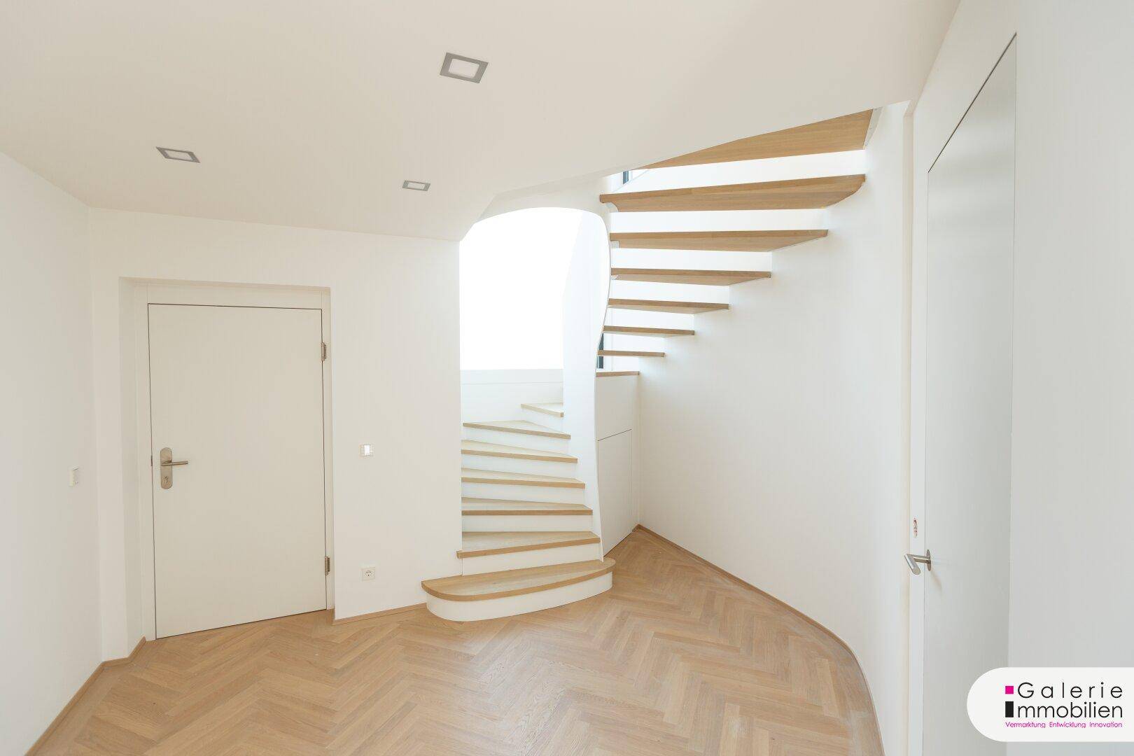 Heller Flur mit eleganter Holzwendeltreppe und modernen Einbaustrahlern in der Decke.