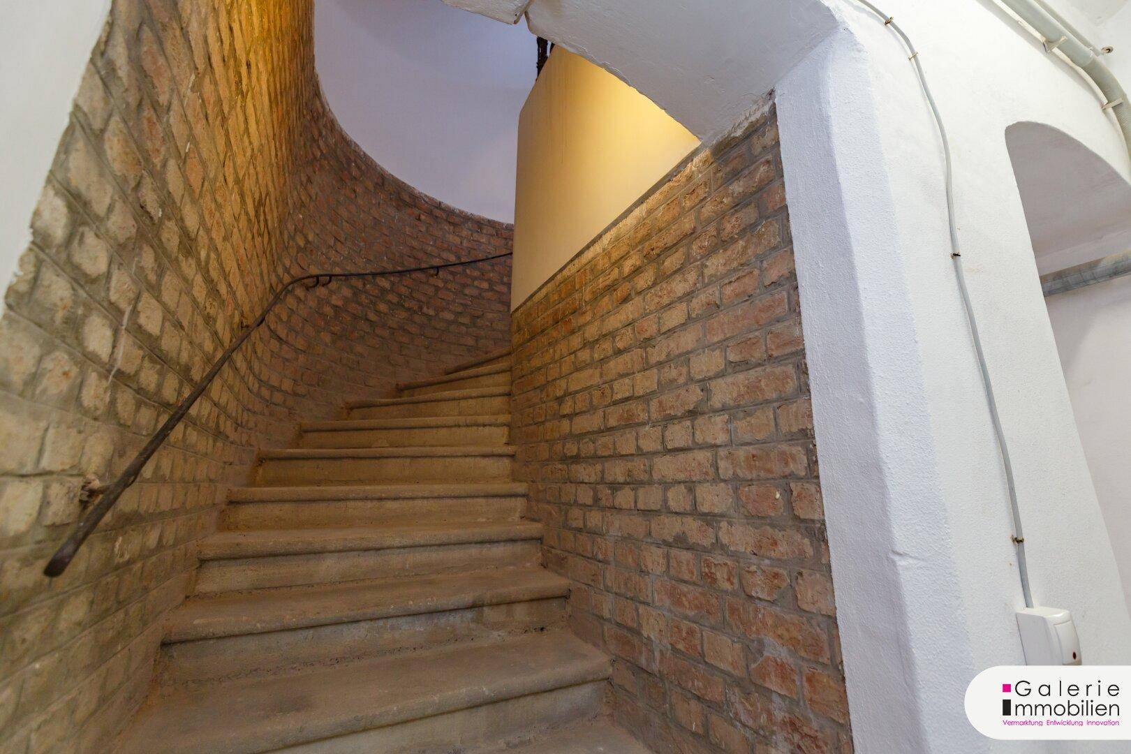 Historisches Treppenhaus mit unverputzten Ziegelwänden und Steinstufen, das den Charme des Altbaus bewahrt.