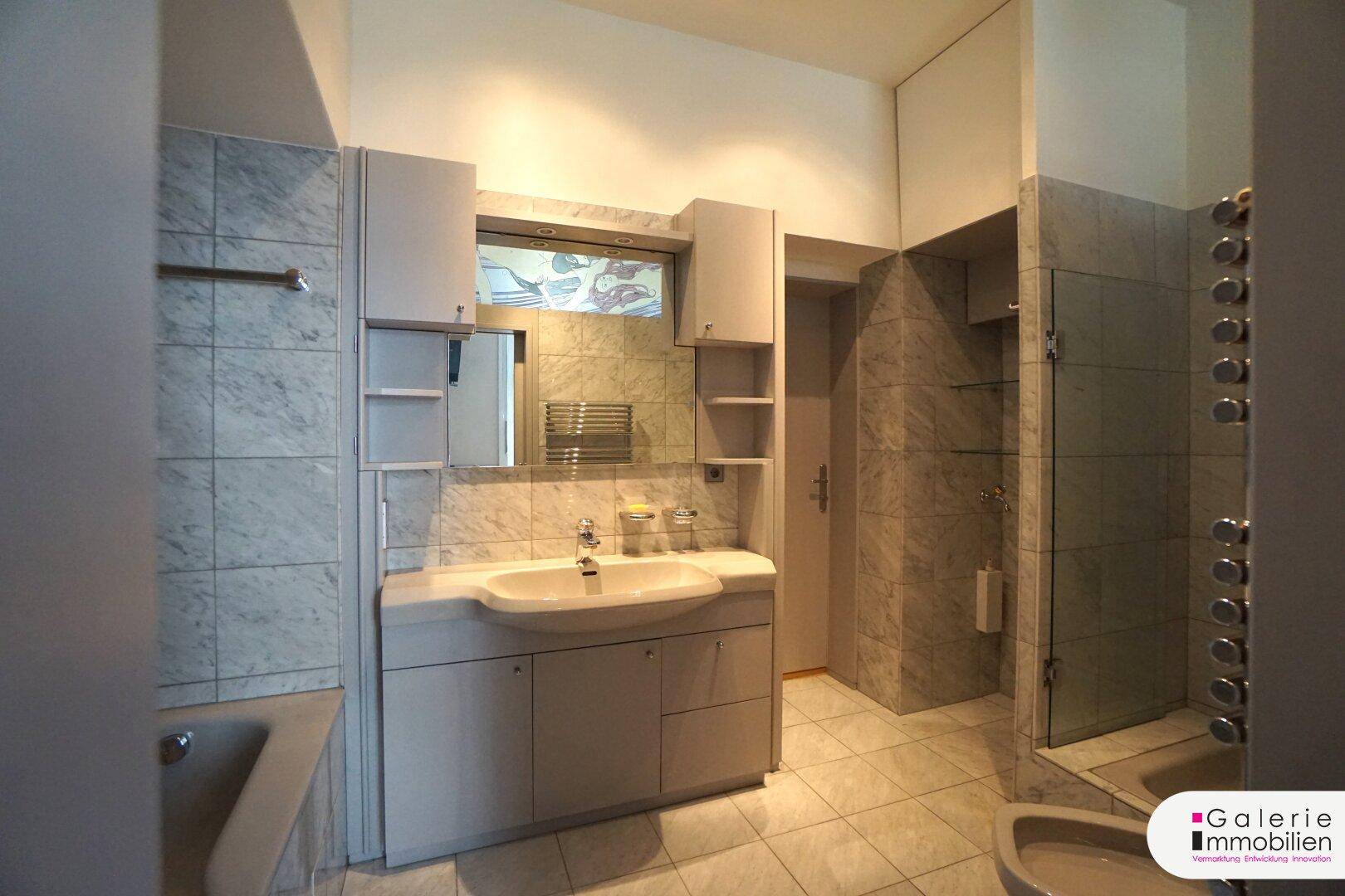 Gefliestes Badezimmer mit Waschtisch, Badewanne und Duschbereich mit Glasabtrennung.