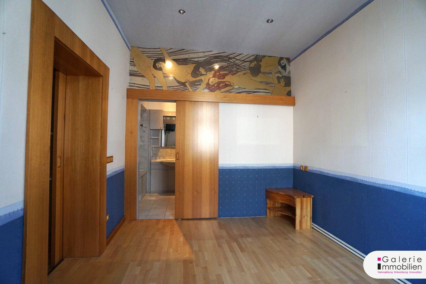 Schlafzimmer mit Holzboden, Schiebetür zum Bad und einer dekorativen Wandmalerei.