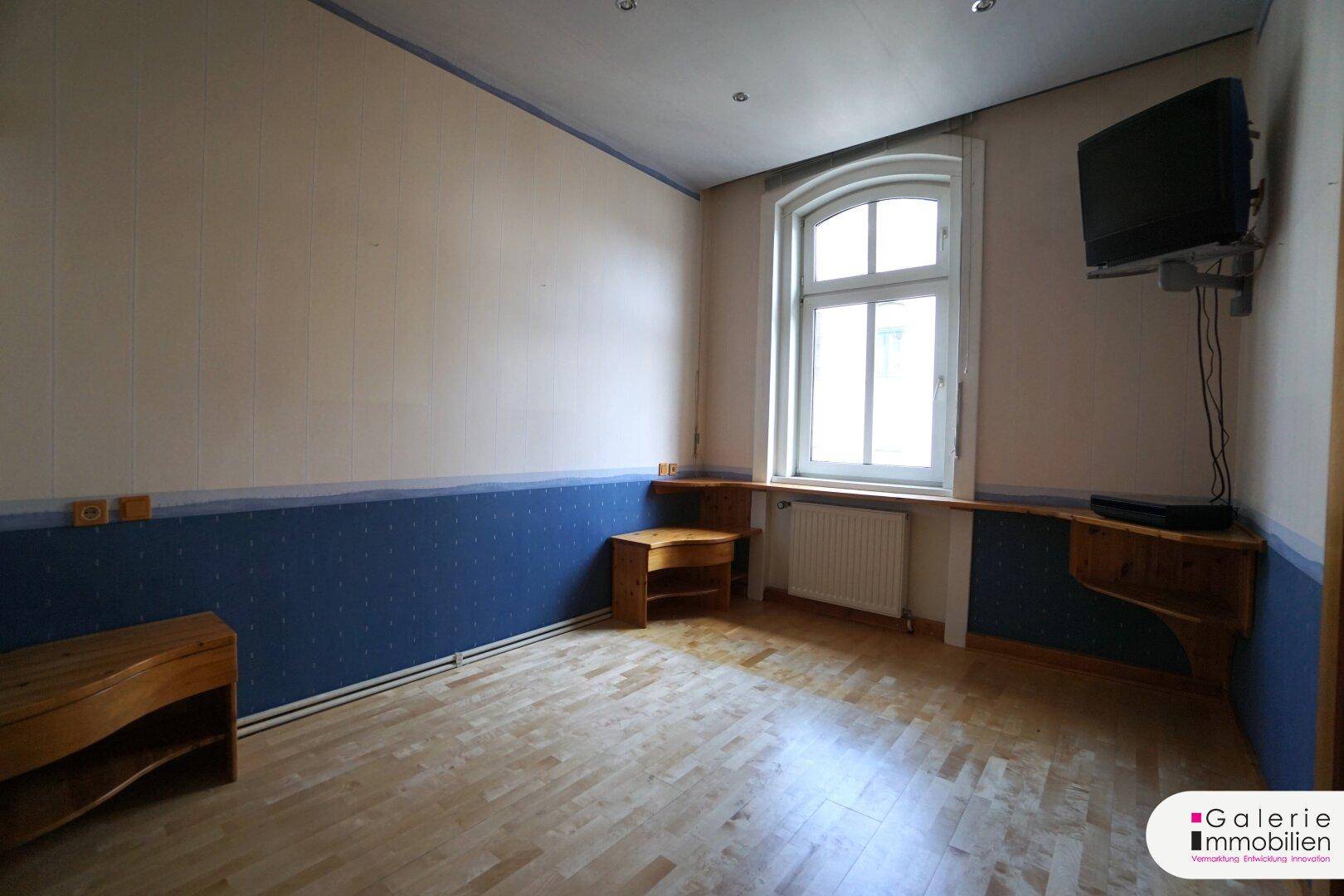 Schlafzimmer mit Holzboden, einem Fenster und einer blau-weißen Wandgestaltung.