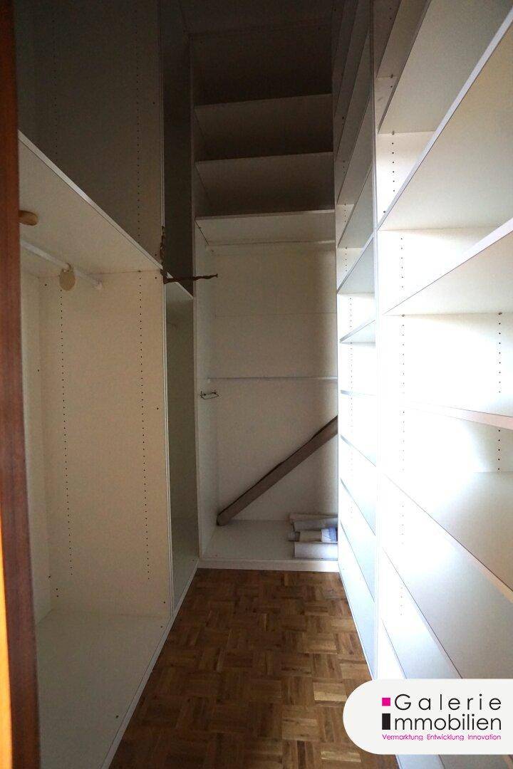 Begehbarer Kleiderschrank mit weißen Regalsystemen und Parkettboden.