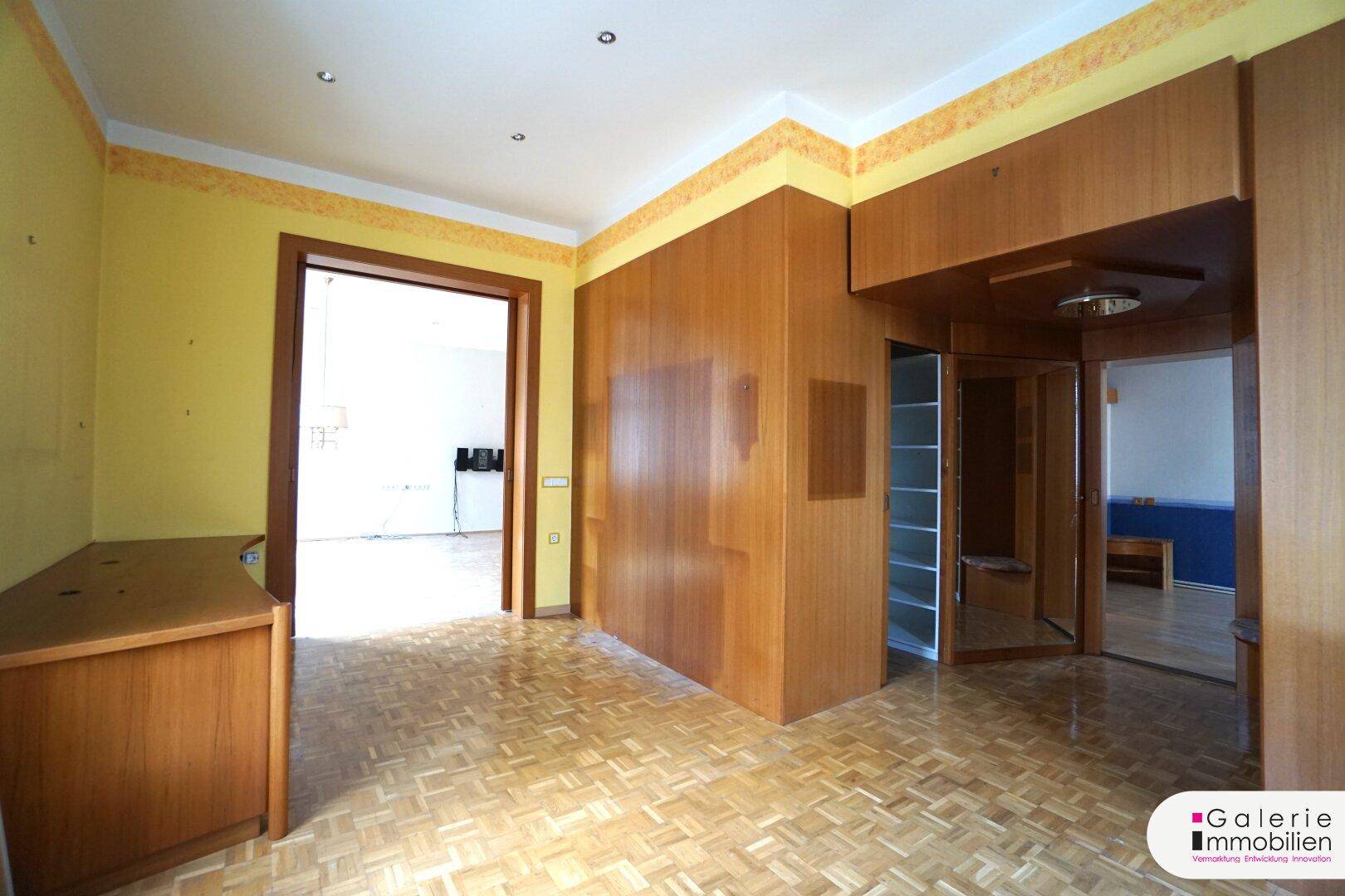Raum mit Parkettboden, eingebauten Holzmöbeln und Zugang zu weiteren Zimmern.
