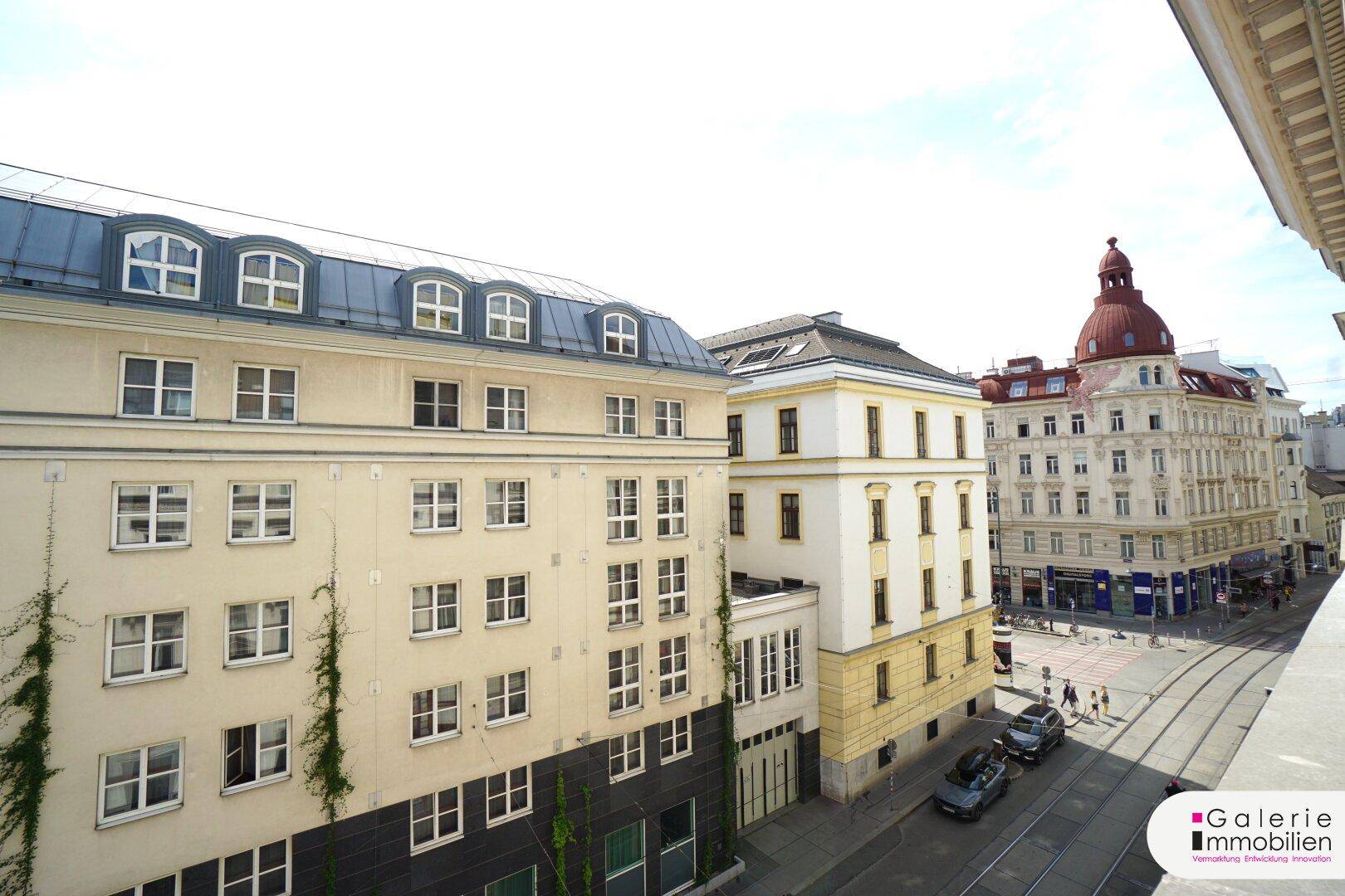 Blick von oben auf eine belebte Stadtstraße mit historischen Gebäuden und einer Straßenbahnlinie.