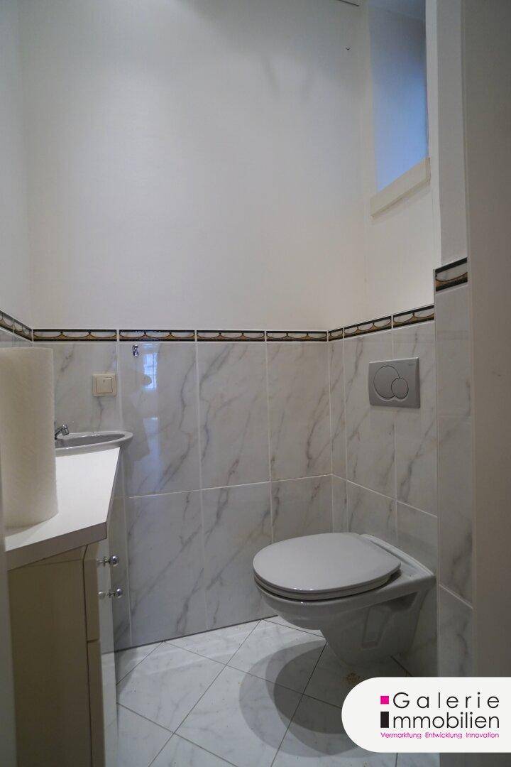 Gäste-WC mit wandhängender Toilette, kleinem Waschbecken und Marmorfliesen.